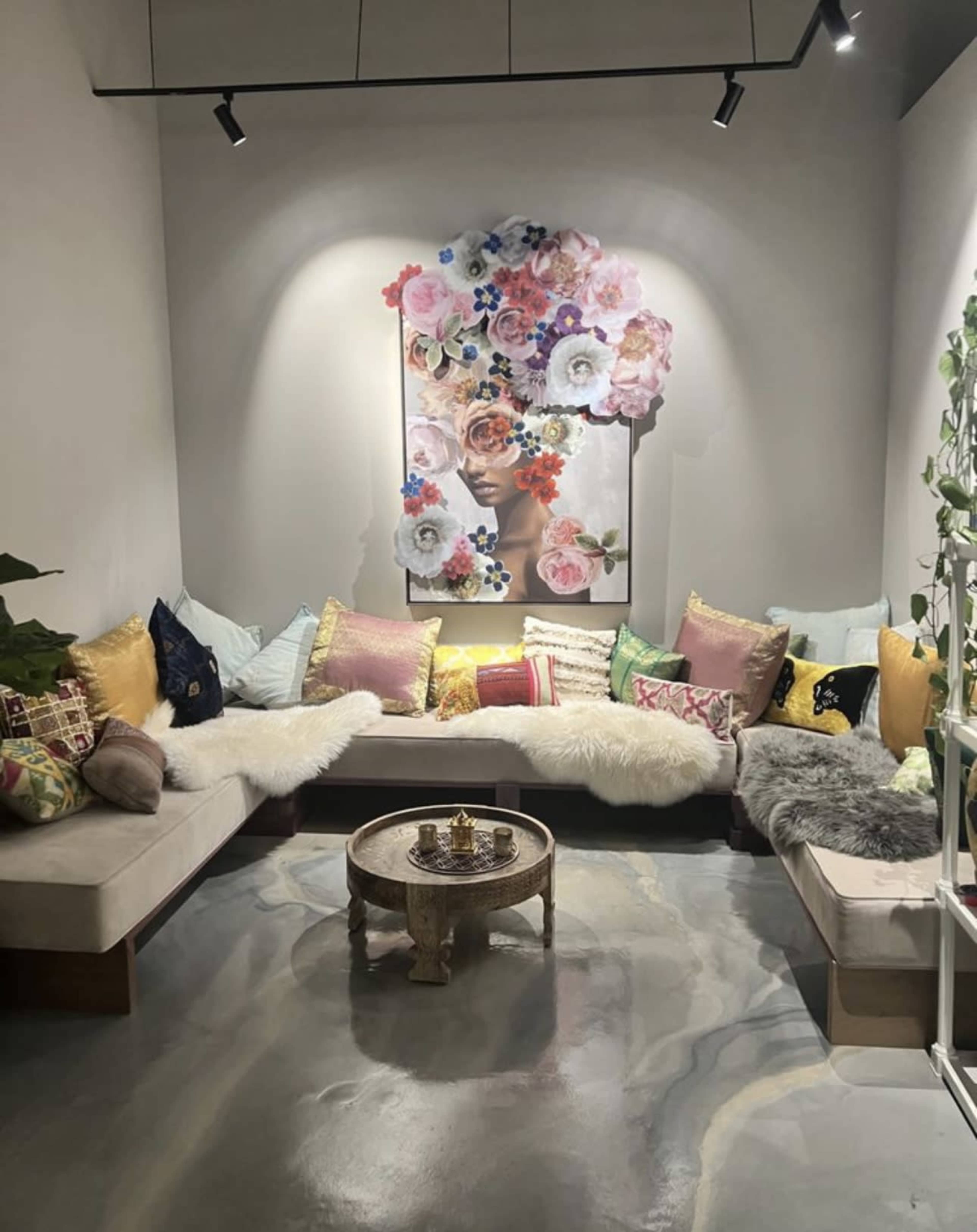 A cozy seating area features a large artwork adorned with flowers, surrounded by colorful cushions and a small wooden table.