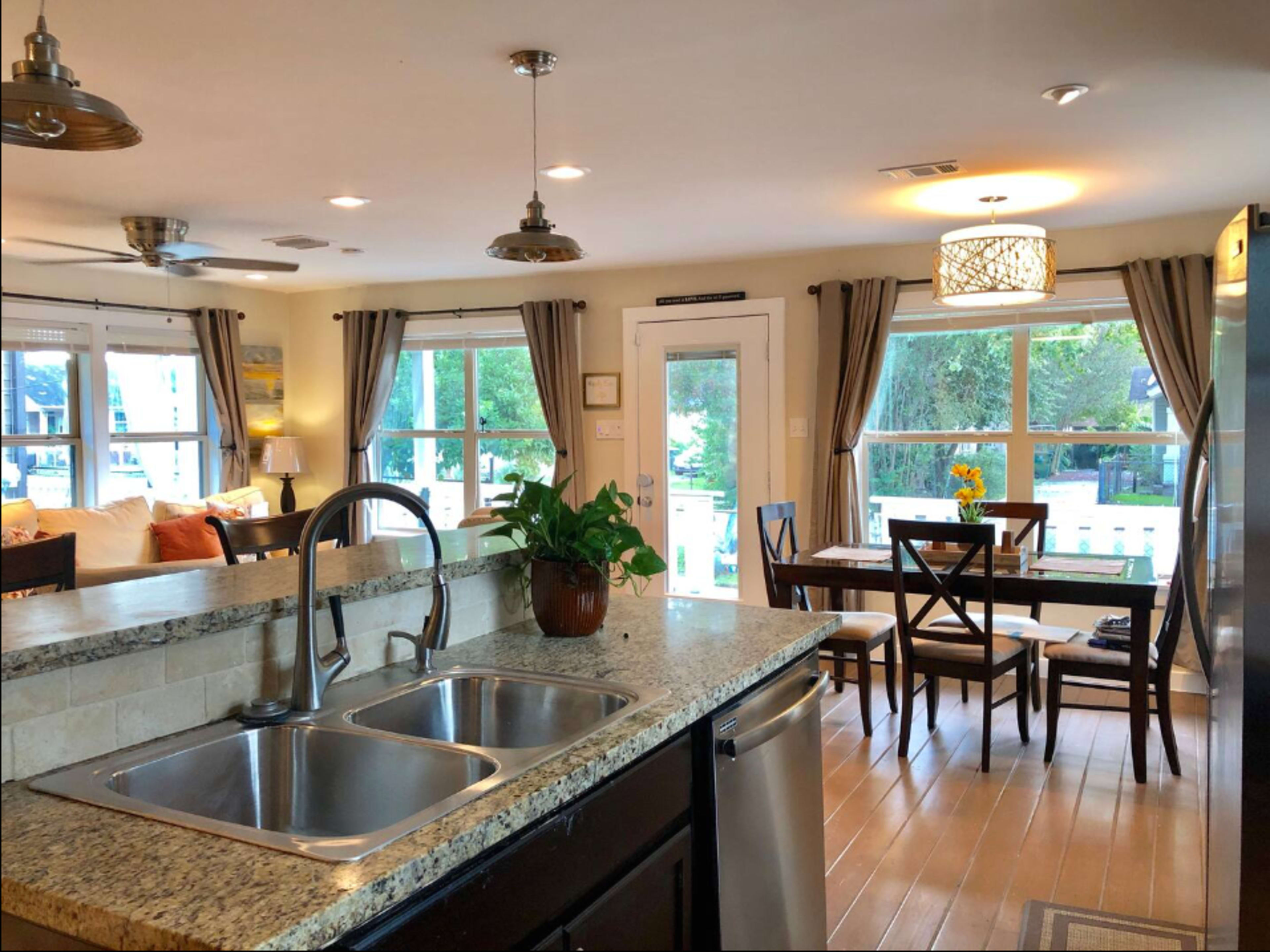 A modern kitchen with granite countertops, stainless steel appliances, and a dining area featuring a wooden table and chairs beside large windows.