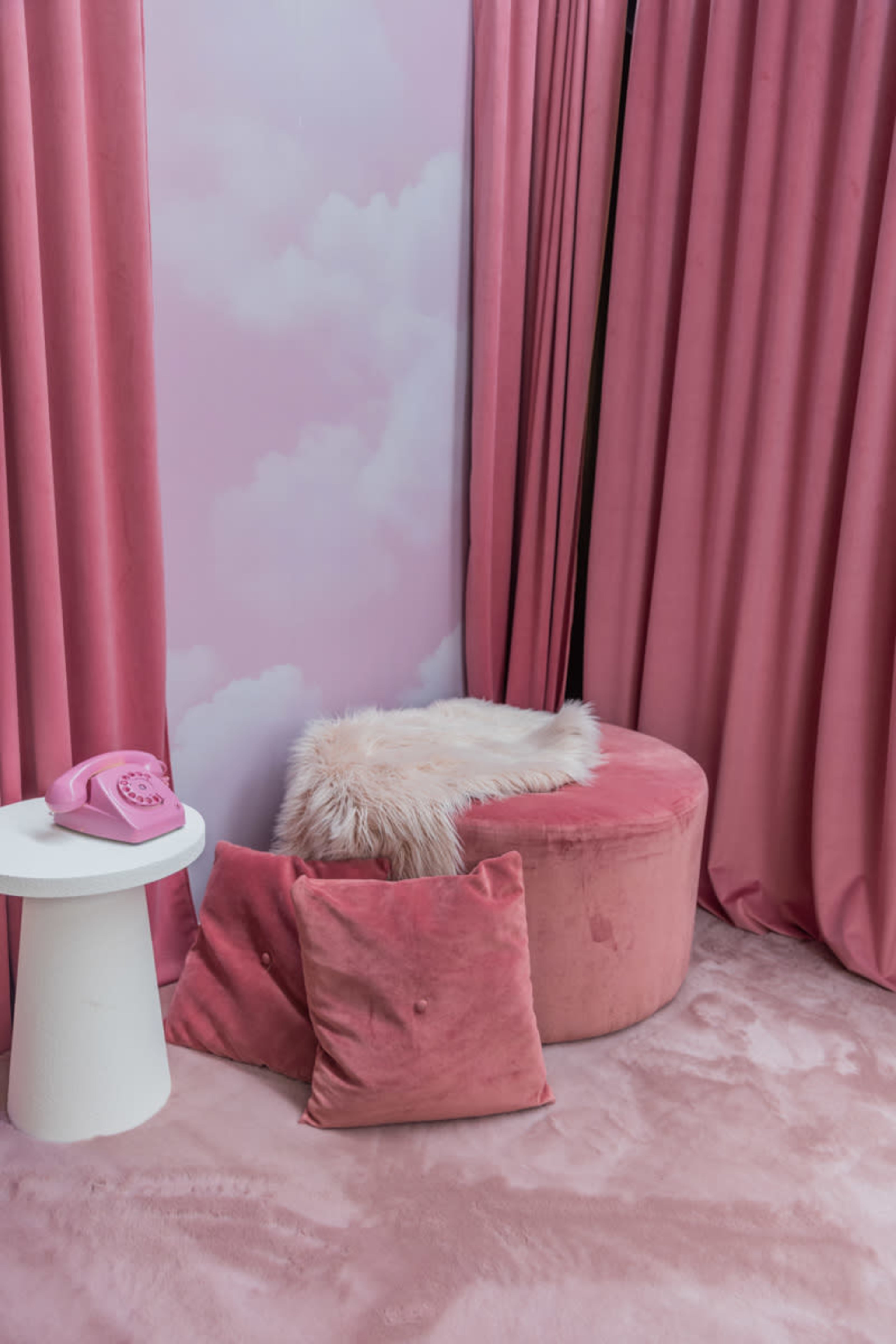 The scene features a soft pink room adorned with velvet curtains, a circular ottoman with a fur throw, and decorative pillows on a plush carpet.