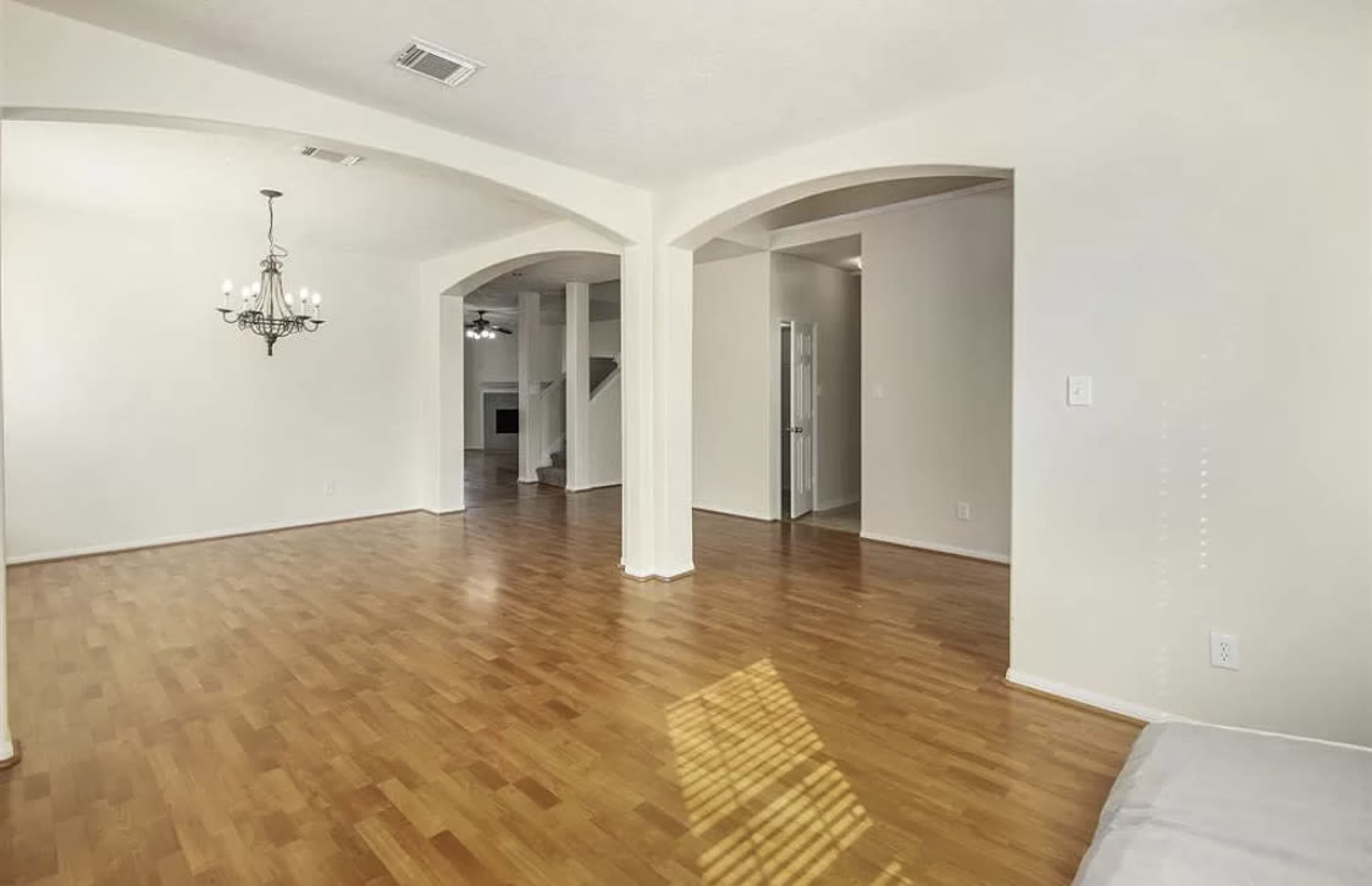 A spacious room with light hardwood flooring, arched doorways, and a chandelier hanging from the ceiling.