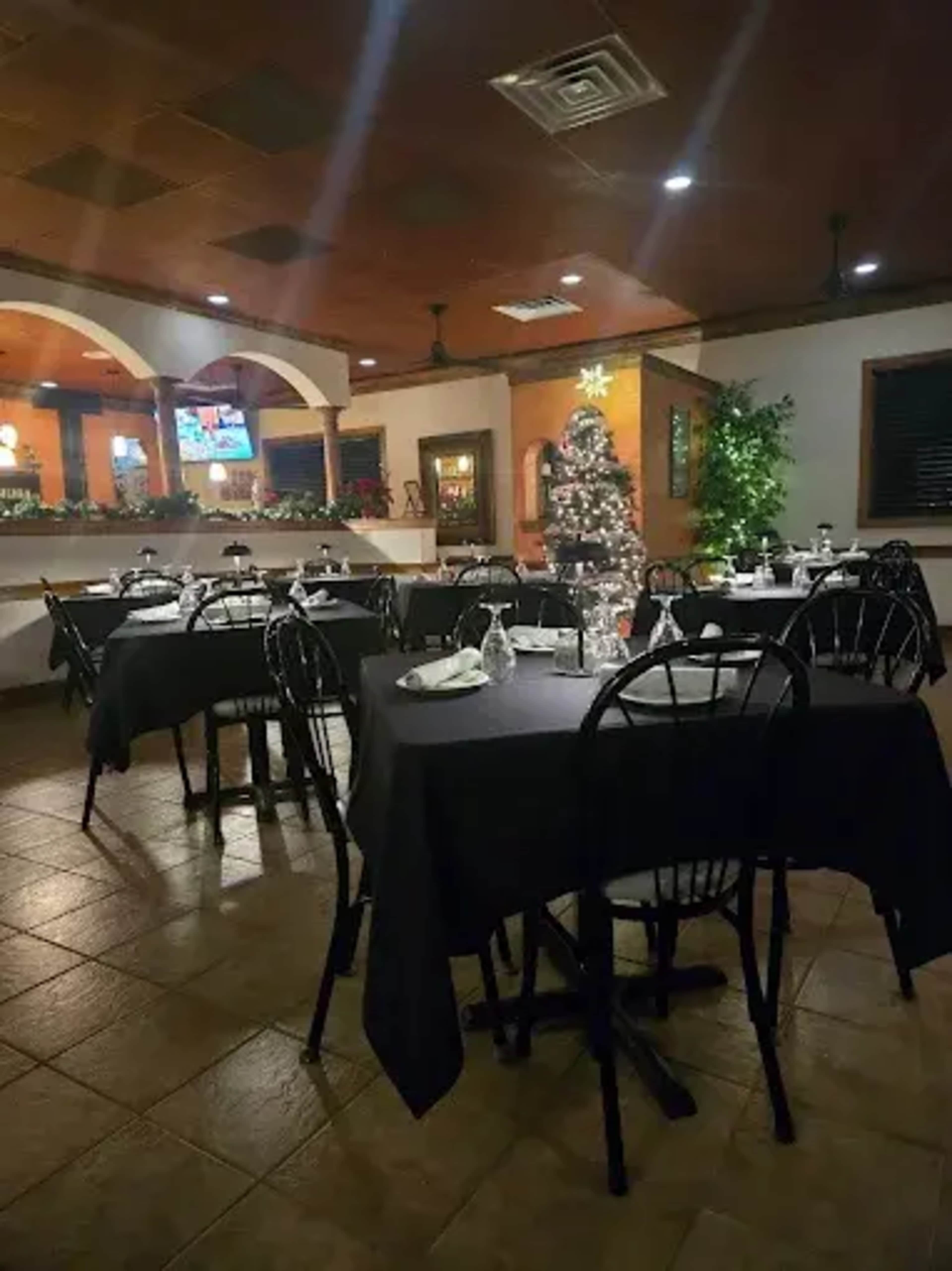 The image shows a dining area in a restaurant with black tablecloths, empty tables, and a decorated Christmas tree in the corner.