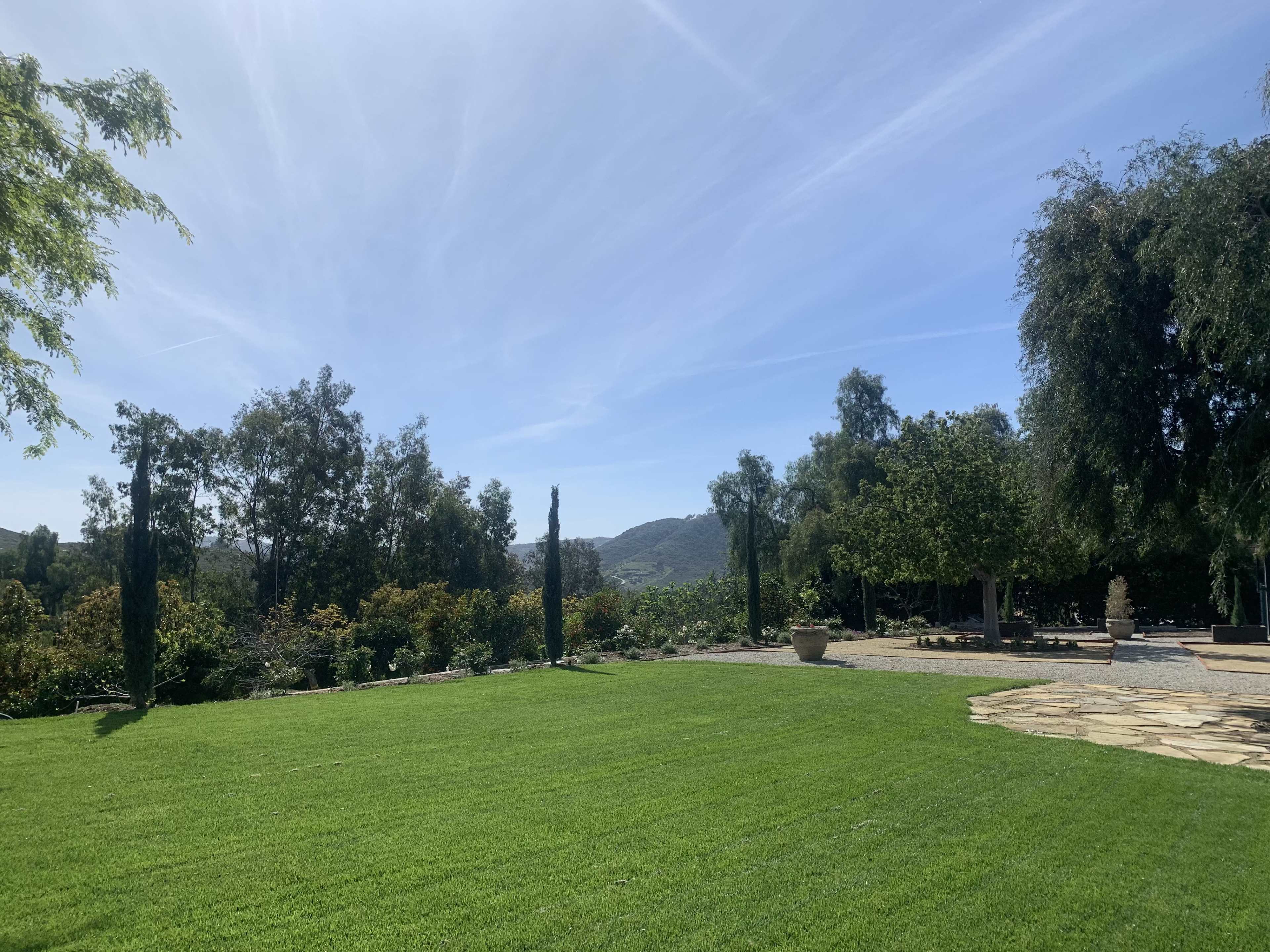 The image shows a spacious green lawn bordered by trees, with distant hills and a clear blue sky in the background.