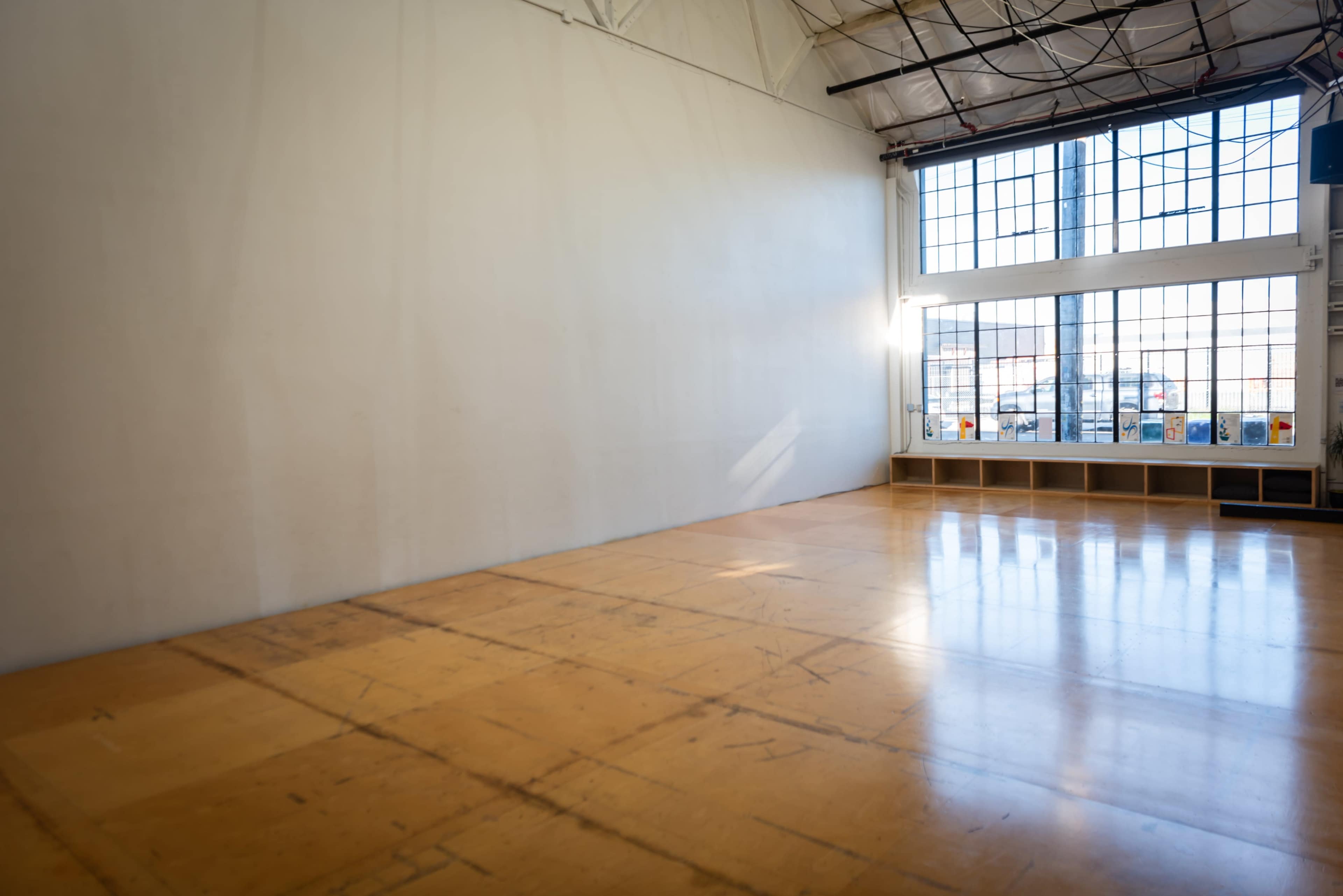 A spacious, empty room with wooden flooring and large windows allowing natural light to enter.