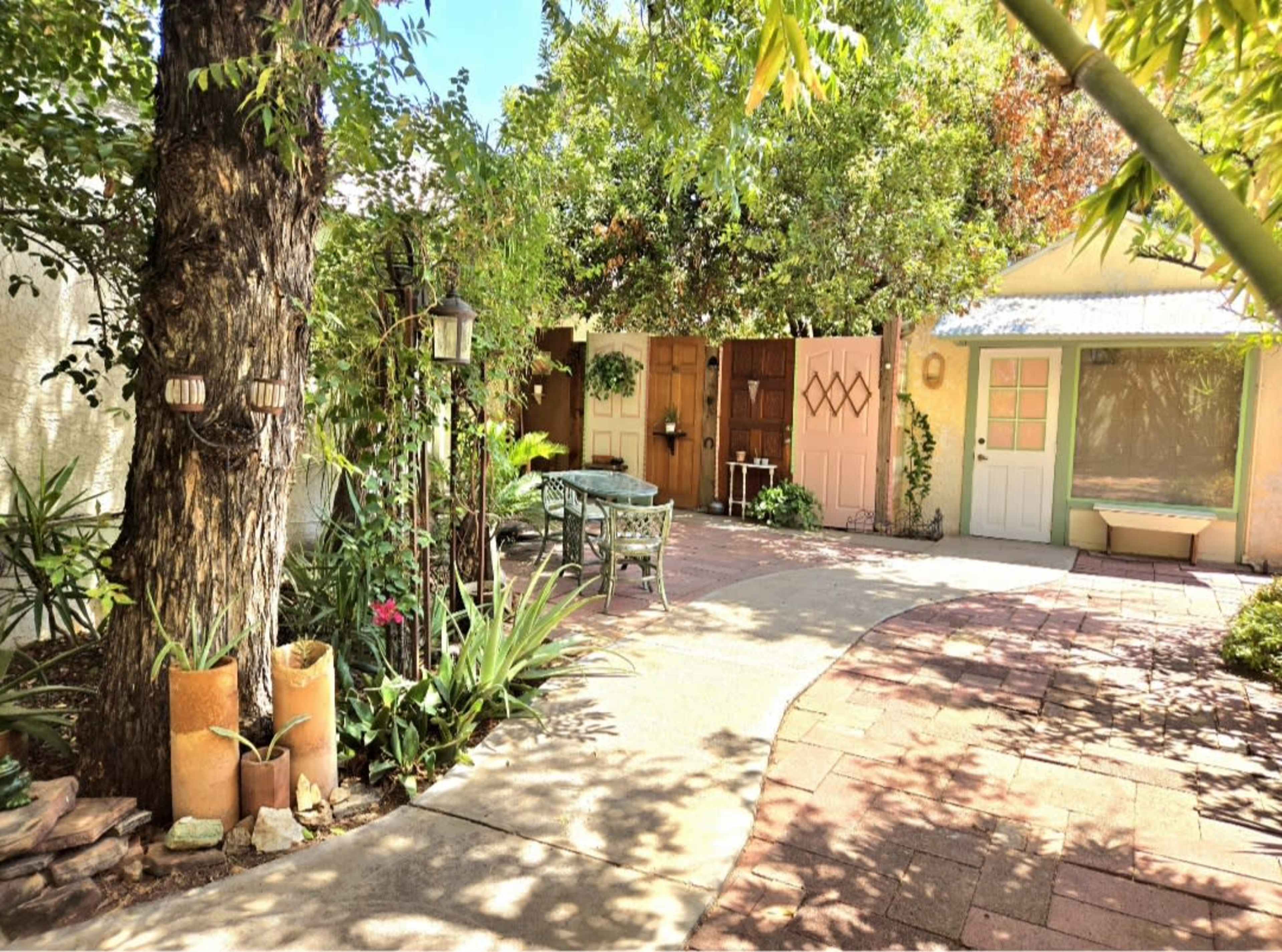 The image shows a landscaped courtyard with a stone pathway, greenery, and multiple doors leading to different spaces.