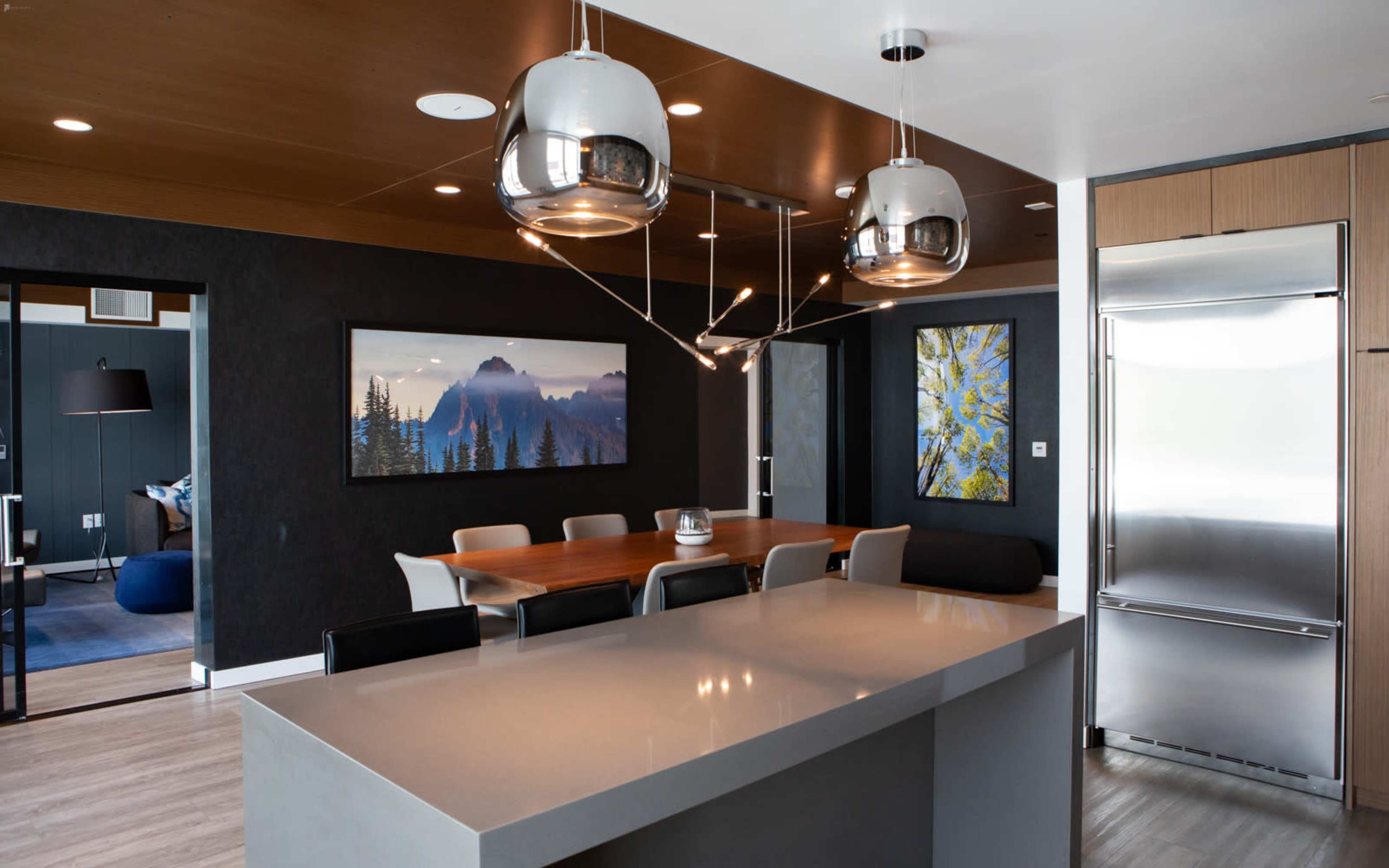 A modern kitchen and dining area with a central island, a wooden dining table, and two framed artworks on the walls.