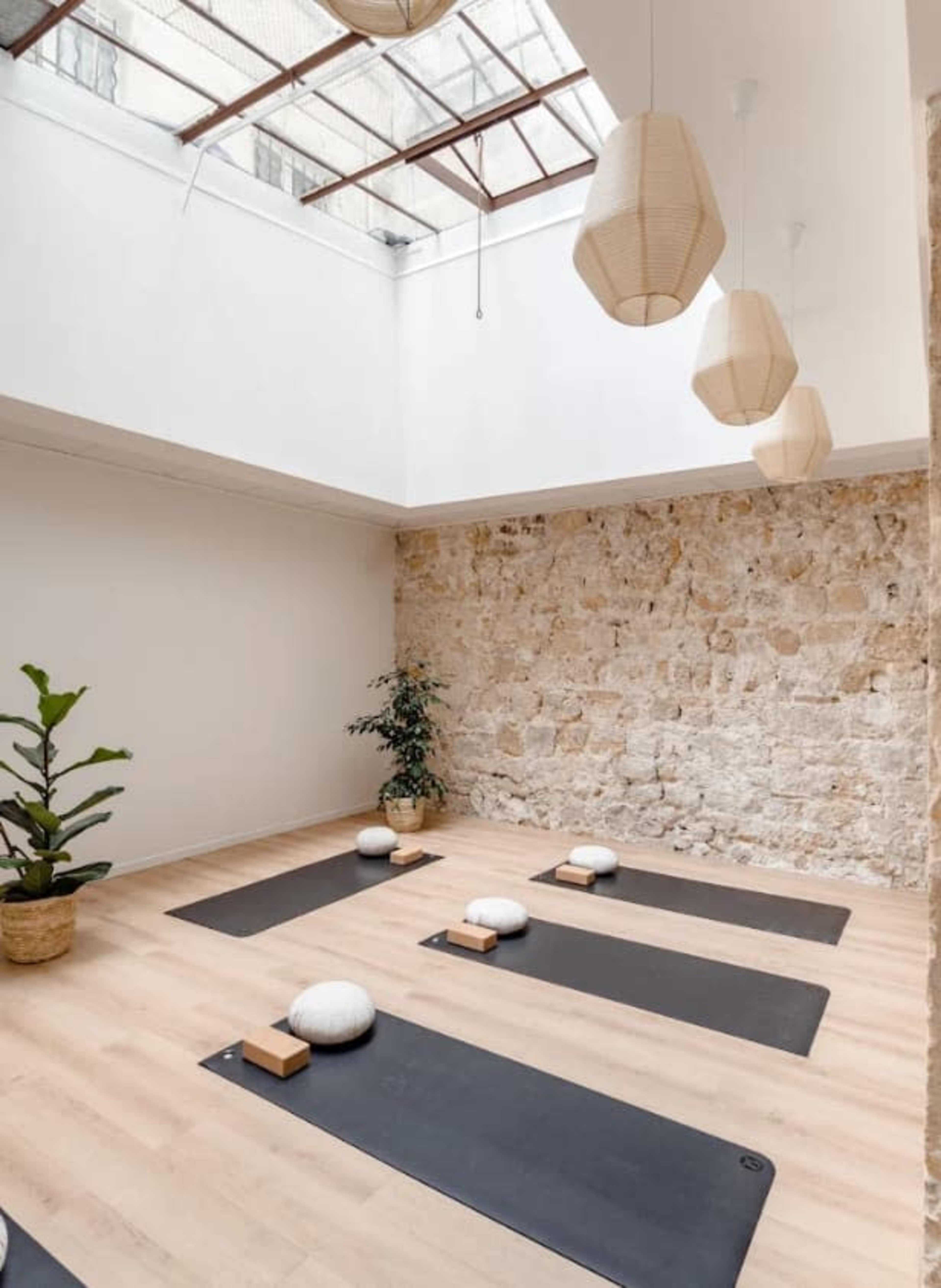 A spacious yoga studio features several yoga mats aligned on a wooden floor beneath a skylight and surrounded by a stone wall.