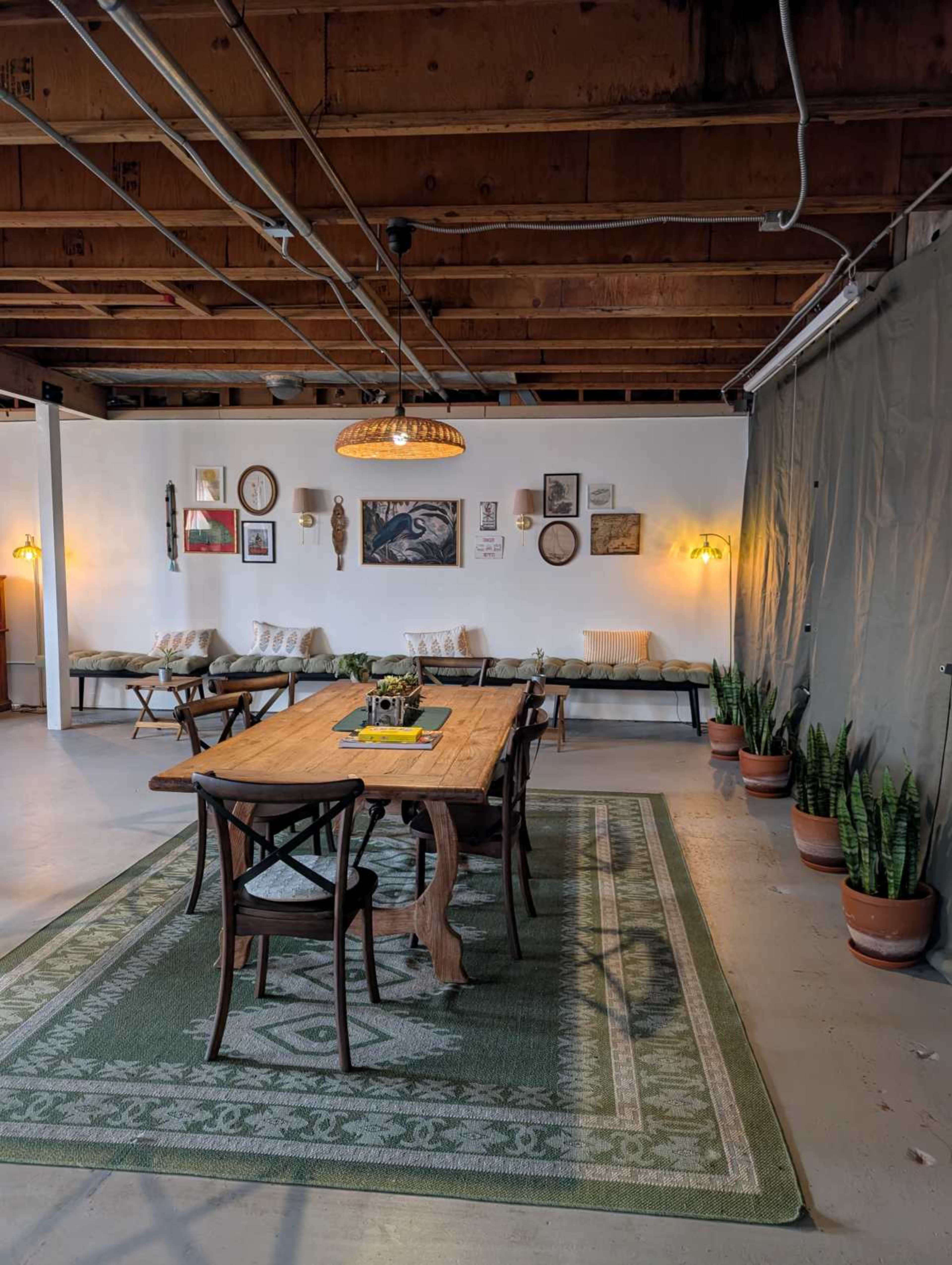 The image shows a spacious dining area with a long wooden table, surrounded by chairs, and walls decorated with various framed artworks.