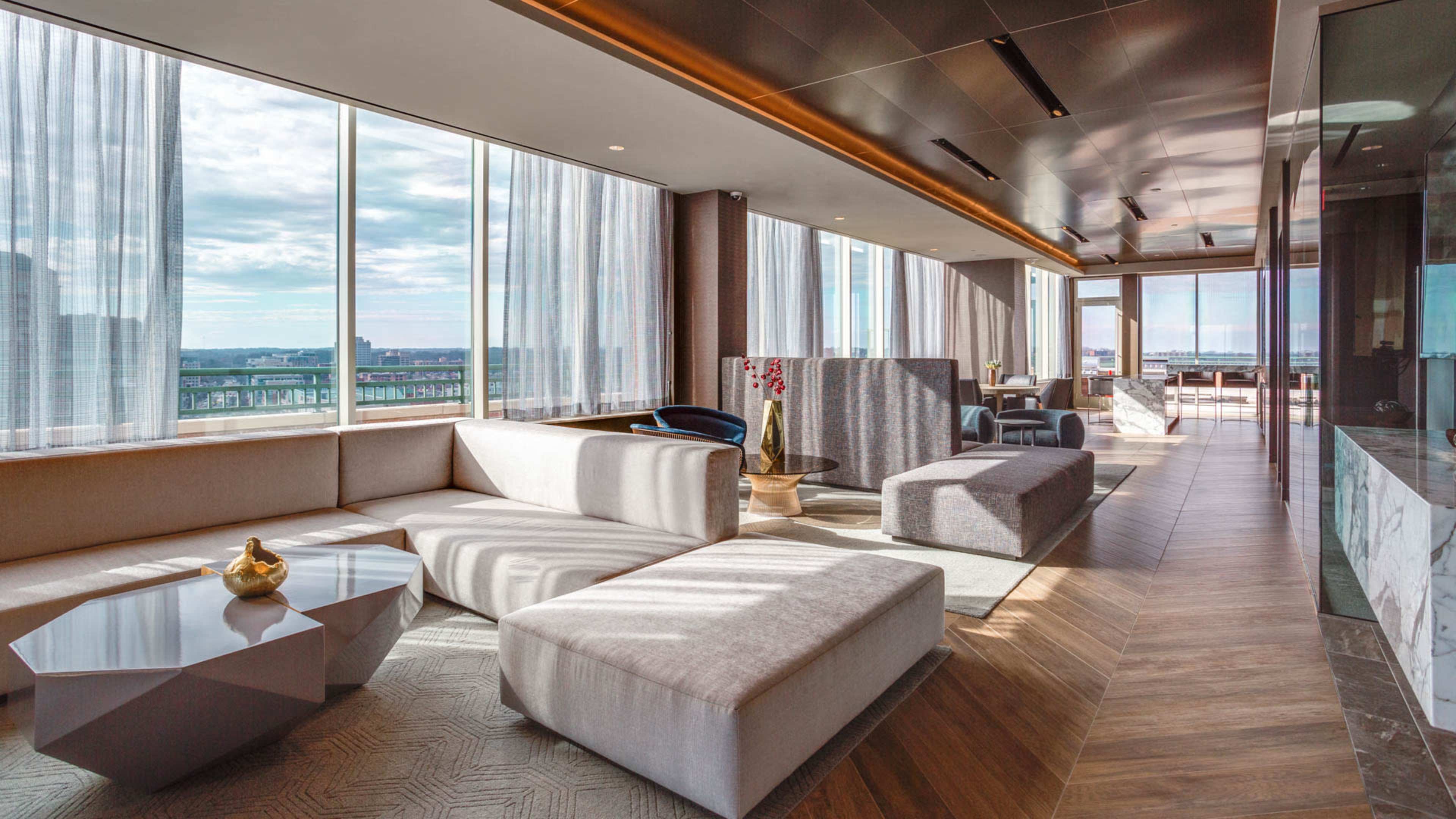 A modern lounge area with large windows, featuring sleek furniture and wooden floors.