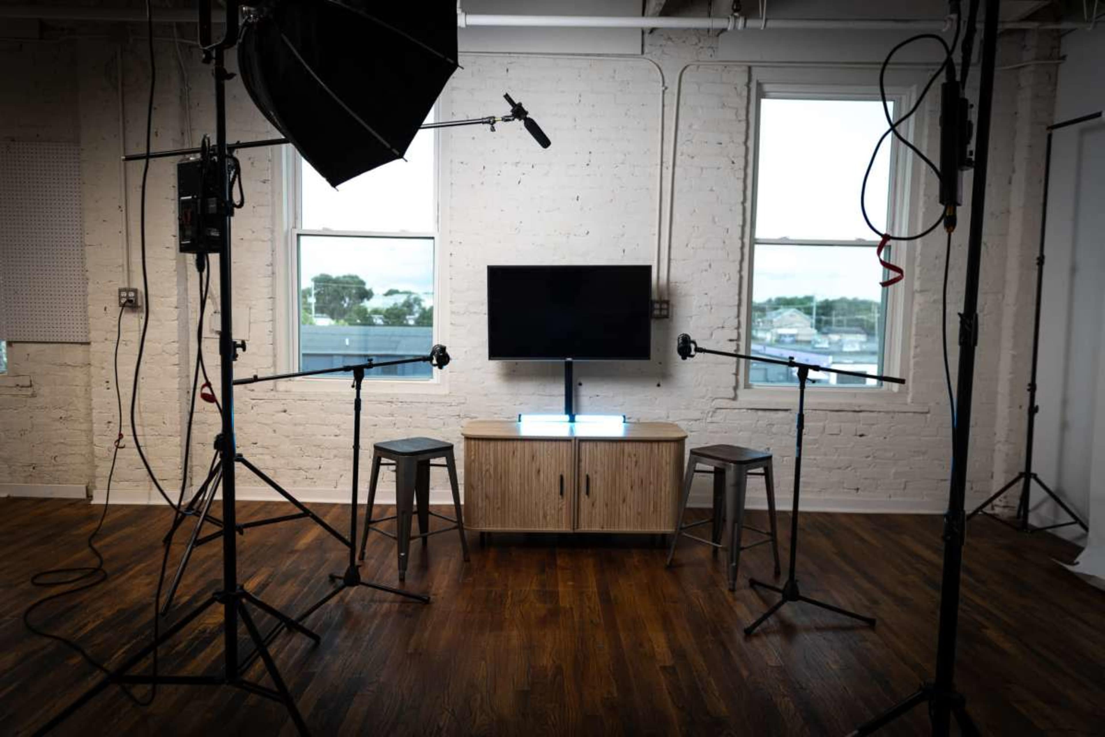 The image shows a well-lit setting with a television mounted on a wooden cabinet surrounded by two stools and various lighting equipment.