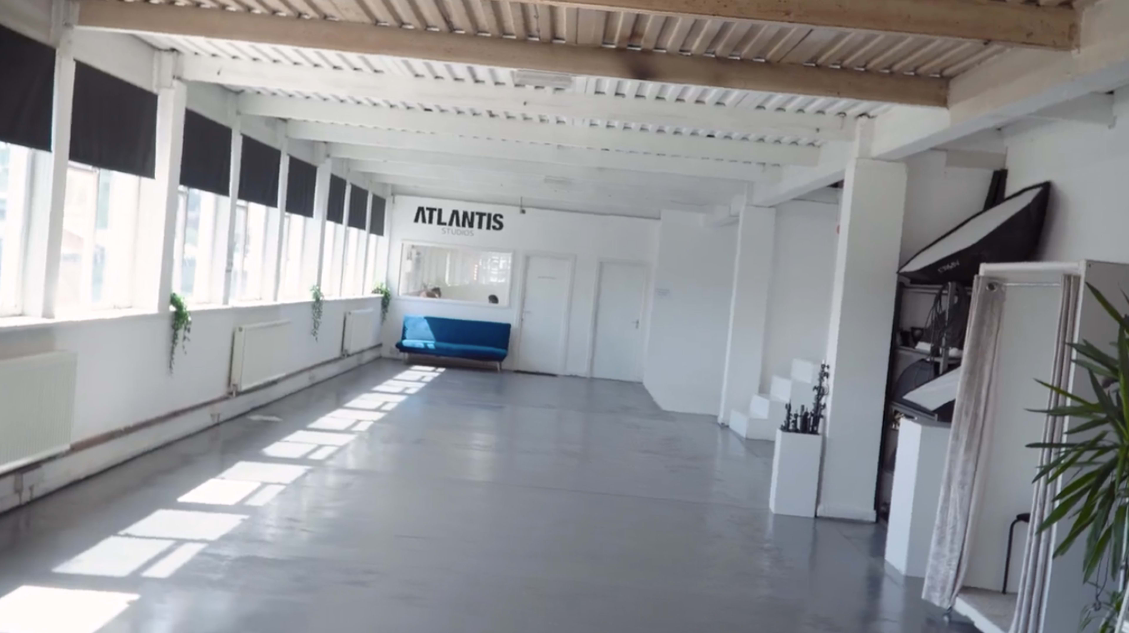 A bright, spacious interior with white walls, polished concrete flooring, and a blue object labeled "ATLANTIS" visible in the background.
