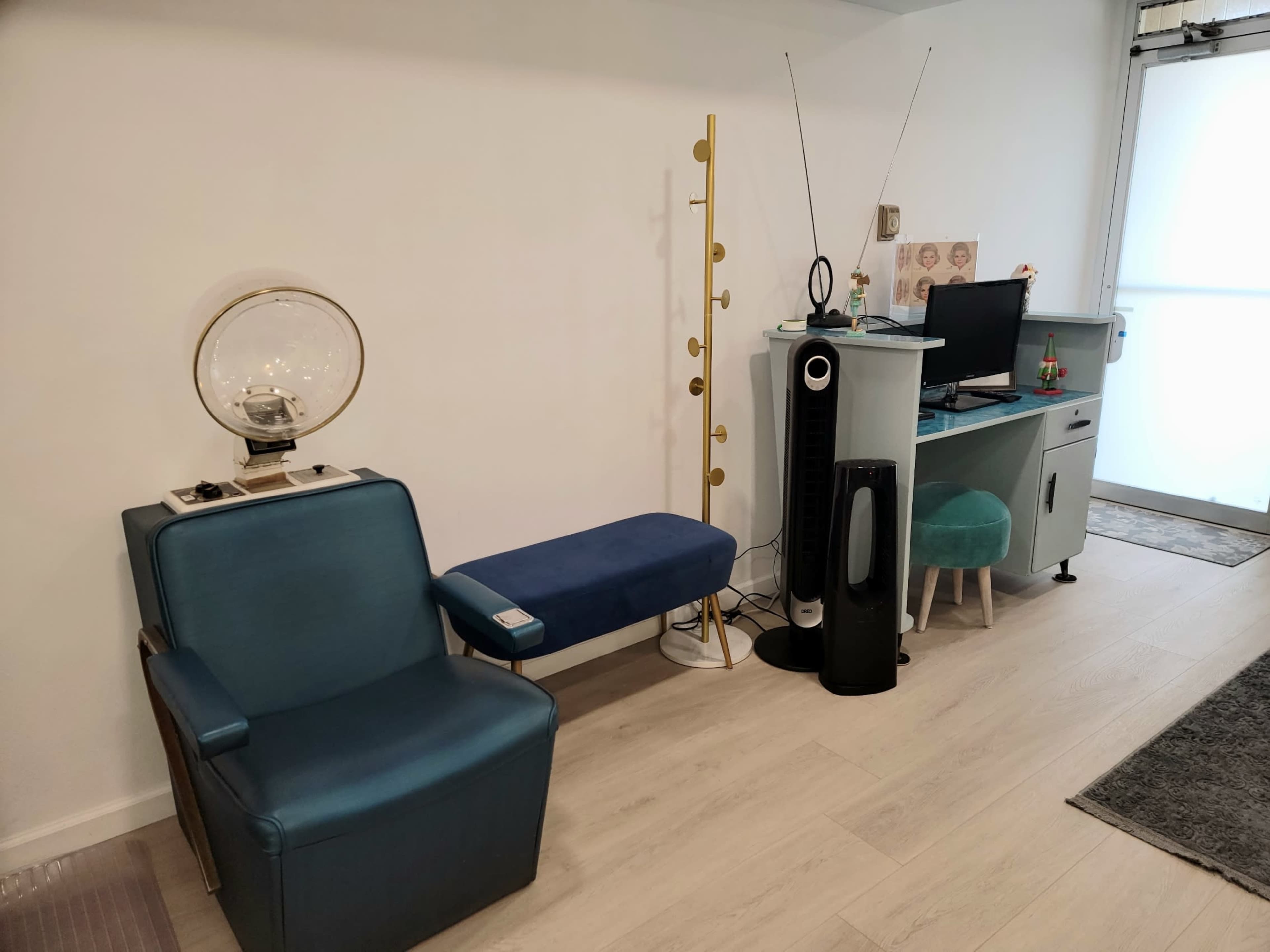 A modern room with a blue chair, a blue bench, a small table with a lamp, a computer setup against a wall, and an air purifier.