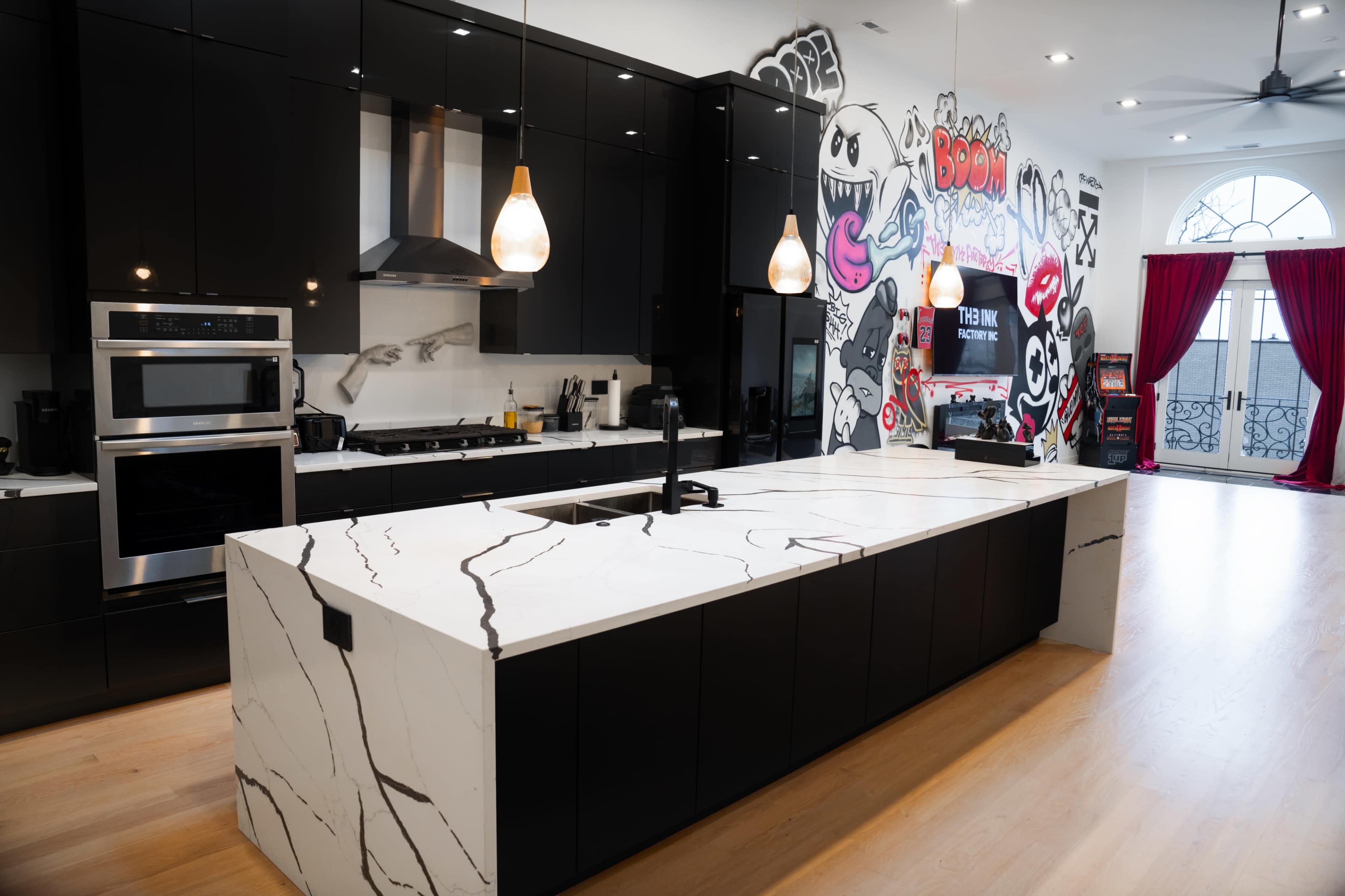 A modern kitchen with black cabinetry, a large marble island, and colorful graffiti artwork on the wall.
