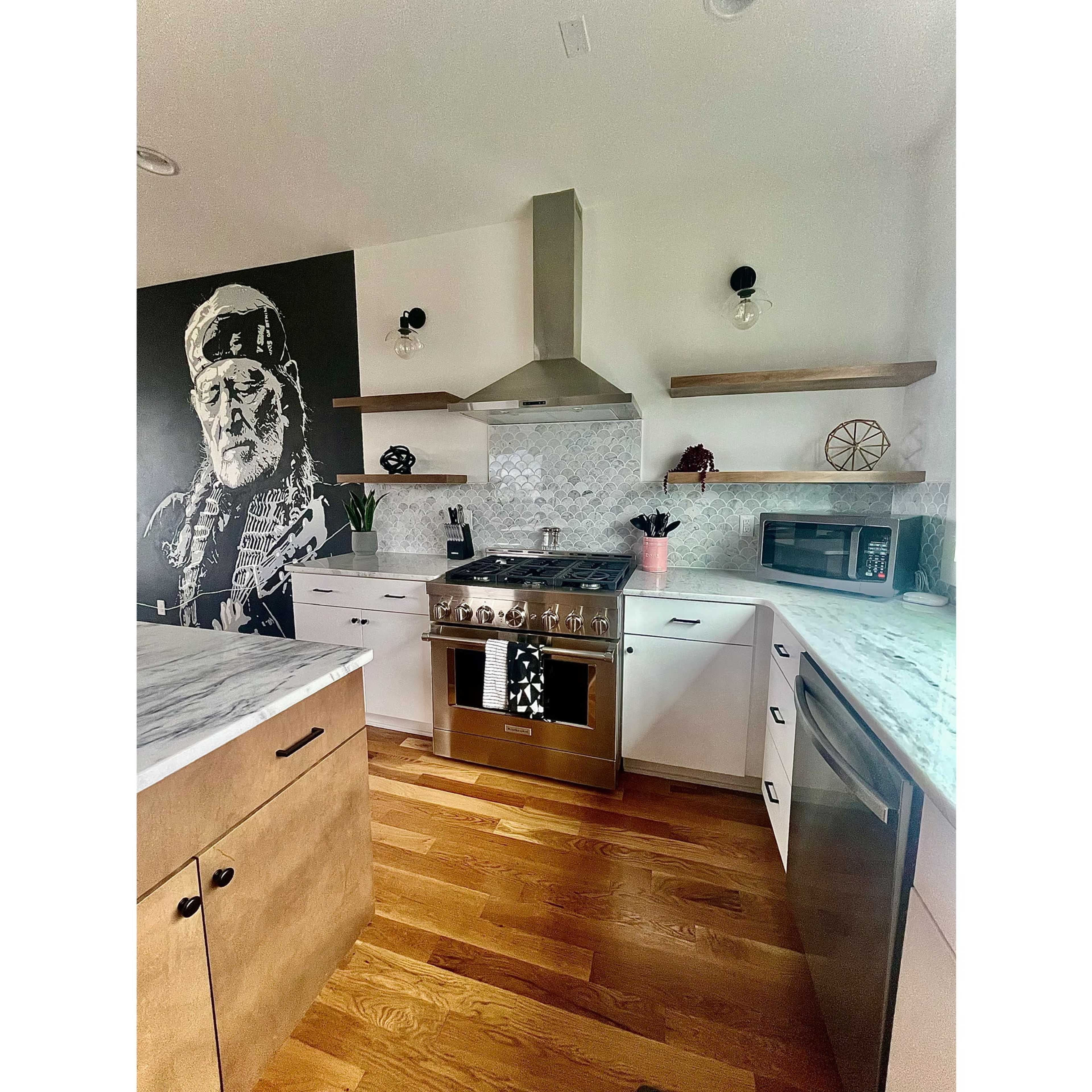 A modern kitchen featuring a stainless steel stove, white cabinets, wooden shelves, and a striking mural of a man on one wall.