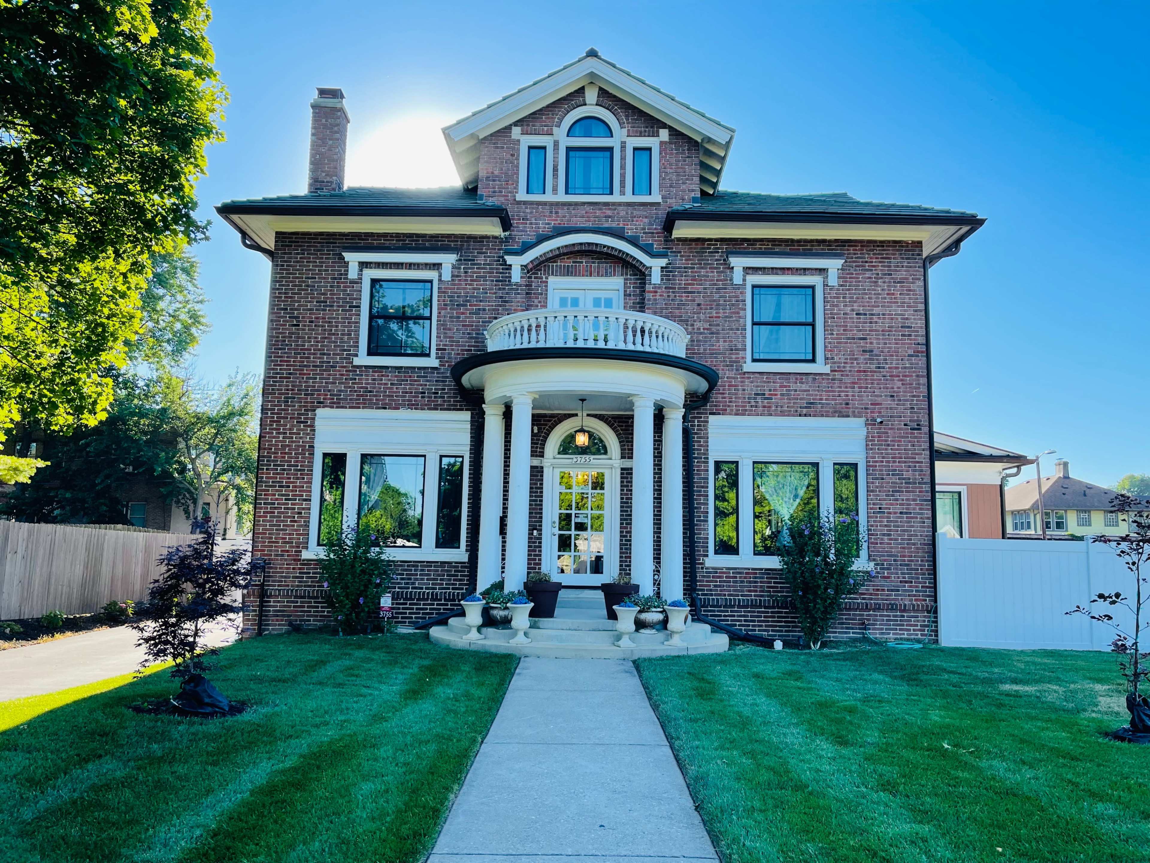 The image shows a large brick house with a prominent front porch and well-maintained landscaping.