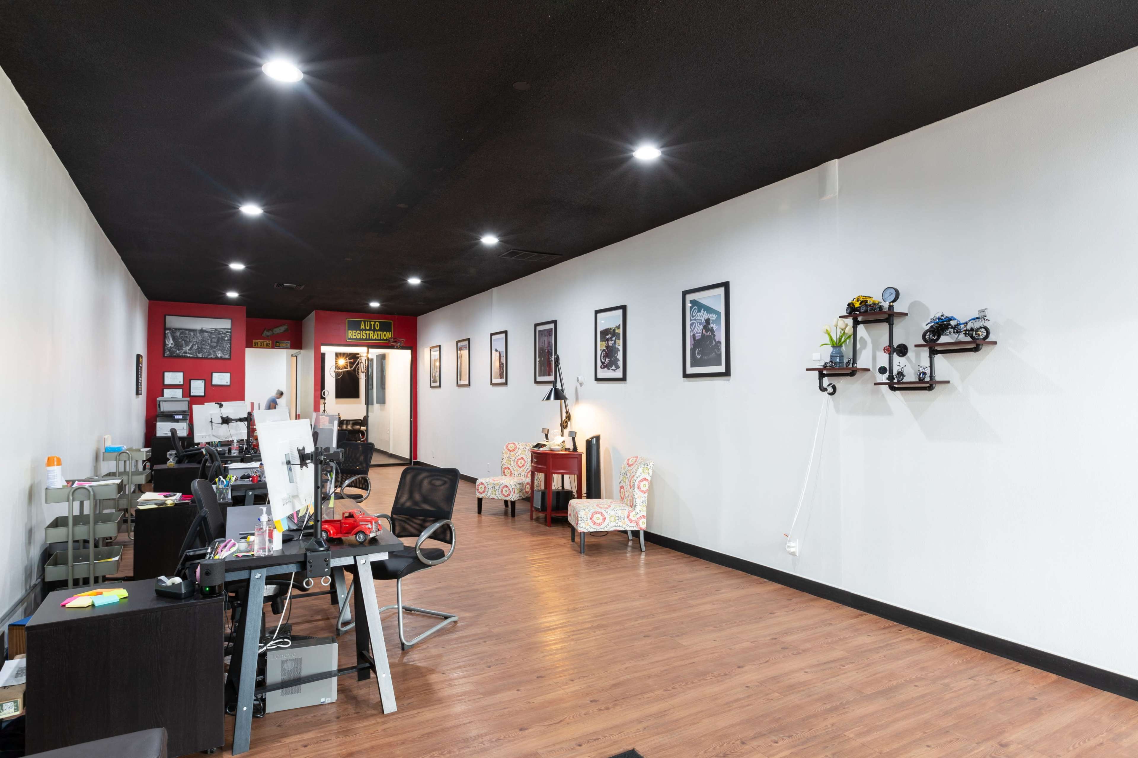 An office space with desks on one side, seating areas with chairs, and framed pictures on the walls.