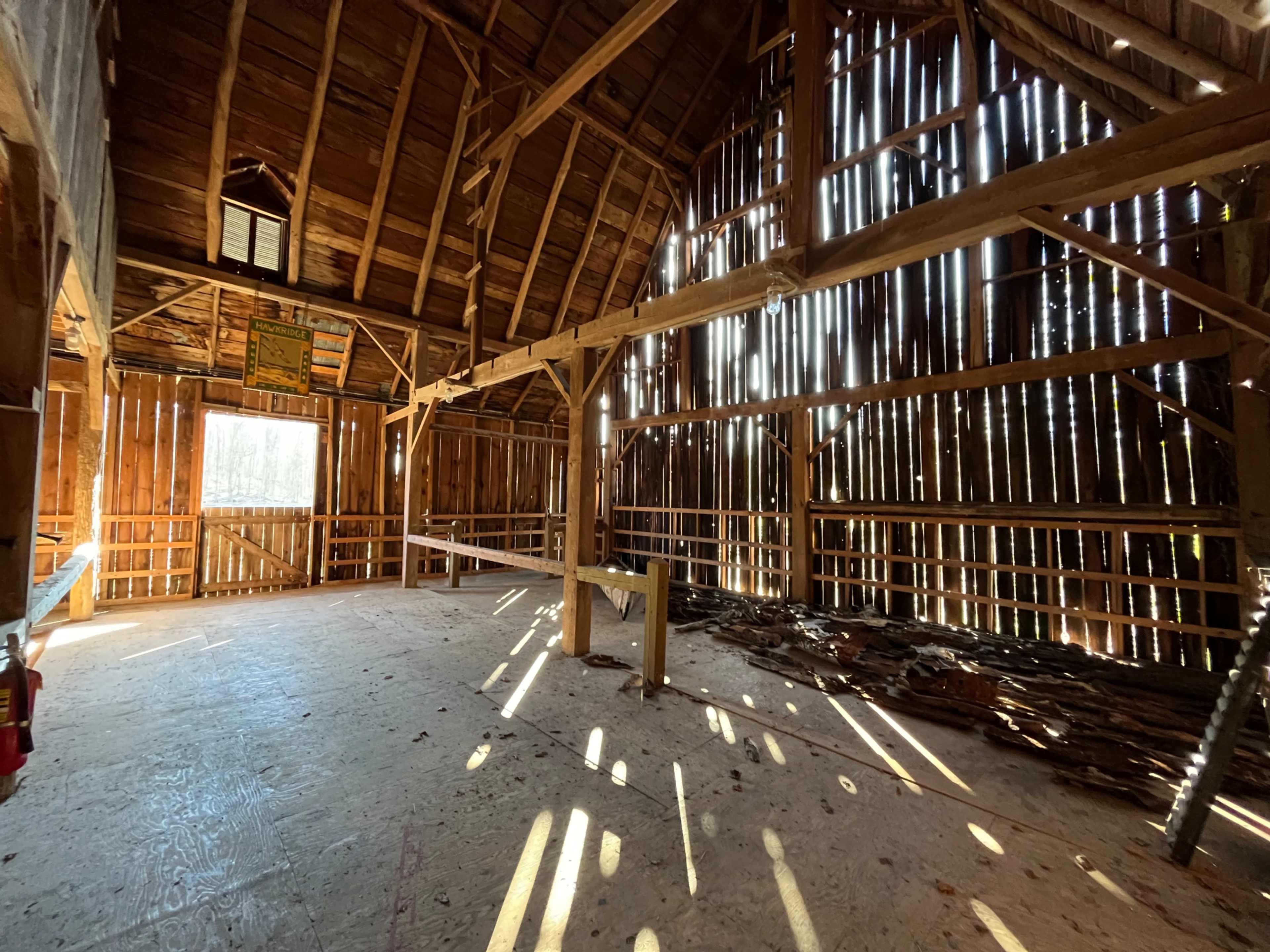 The interior of a rustic barn with wooden beams and sunlight streaming through gaps in the walls.
