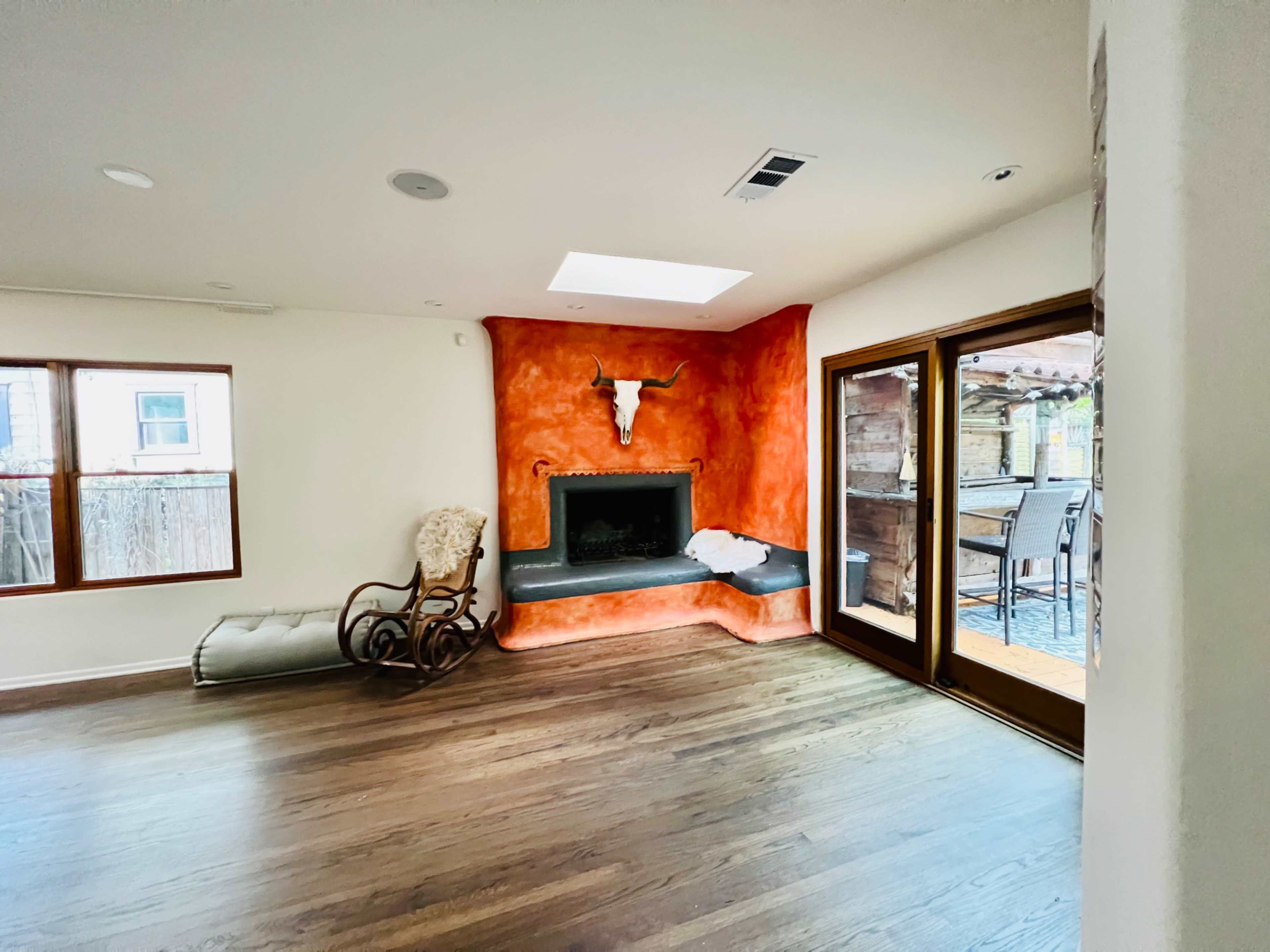 A living room with a large fireplace featuring a bull's head mounted on the orange wall, hardwood floors, and sliding glass doors leading to an outdoor patio area.