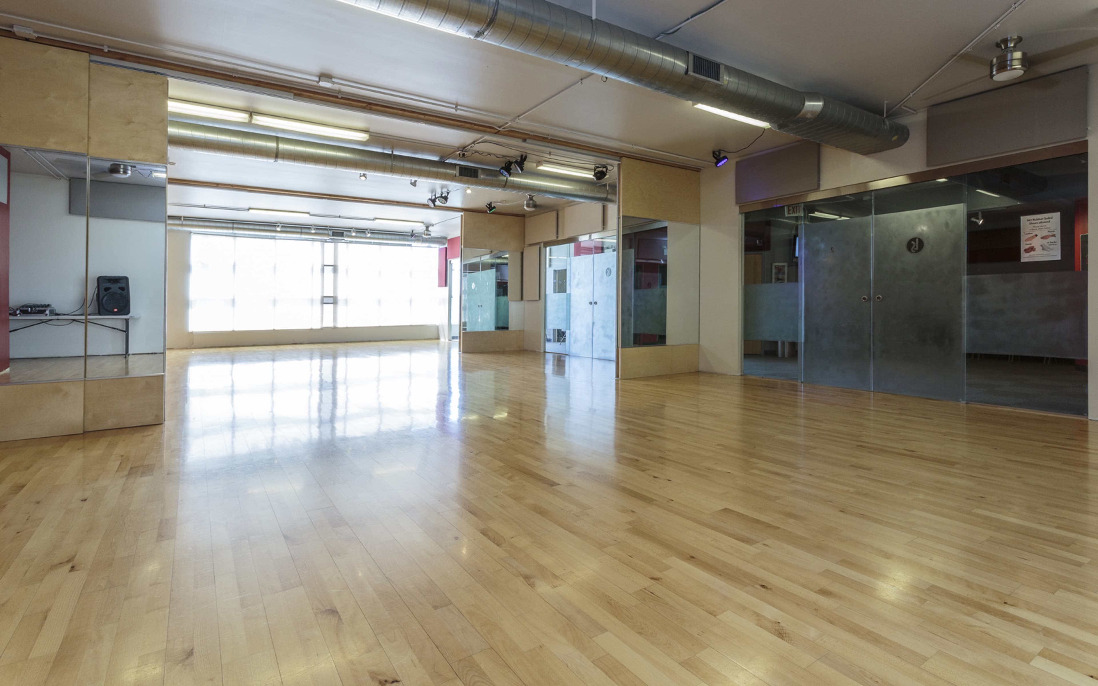 A spacious dance studio with wooden flooring and large mirrors on the walls.