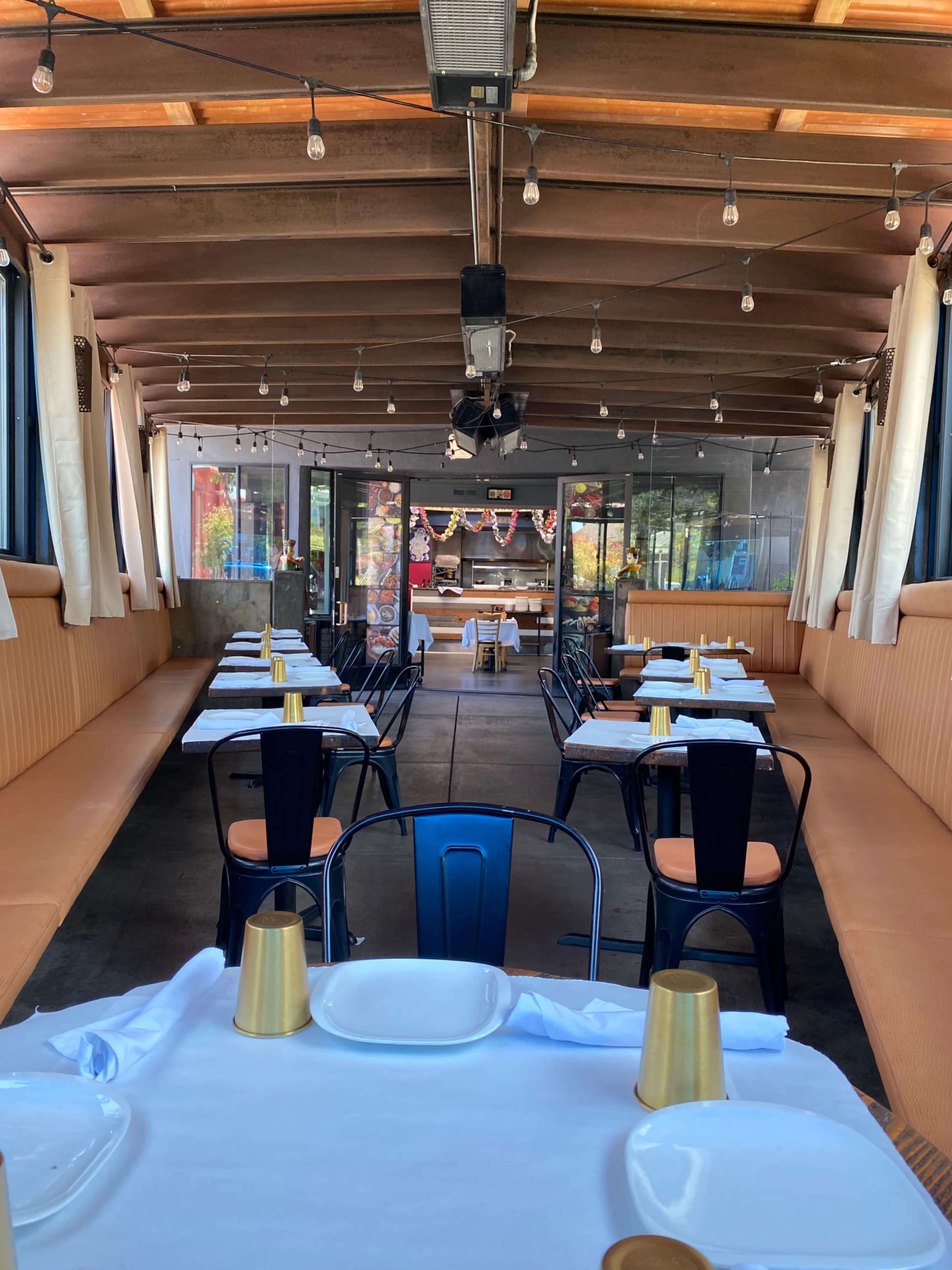 A spacious restaurant interior with tables set for dining and string lights overhead.