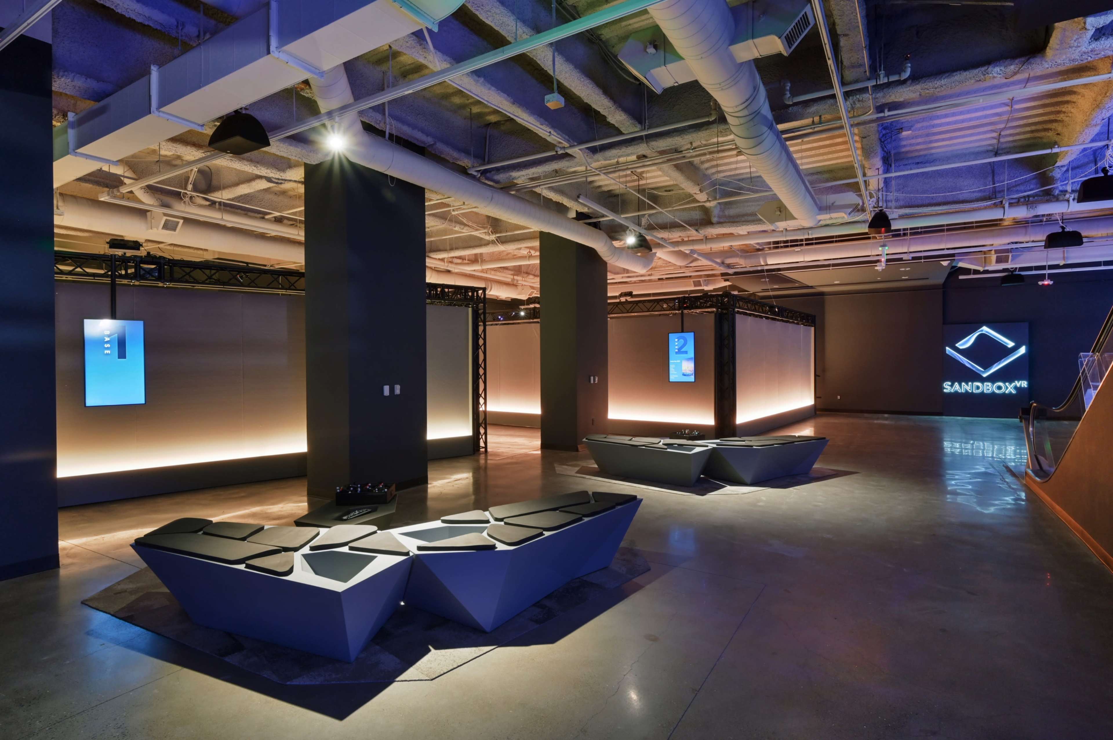 A modern, minimalist lounge area with angular seating and illuminated display panels in a spacious interior.
