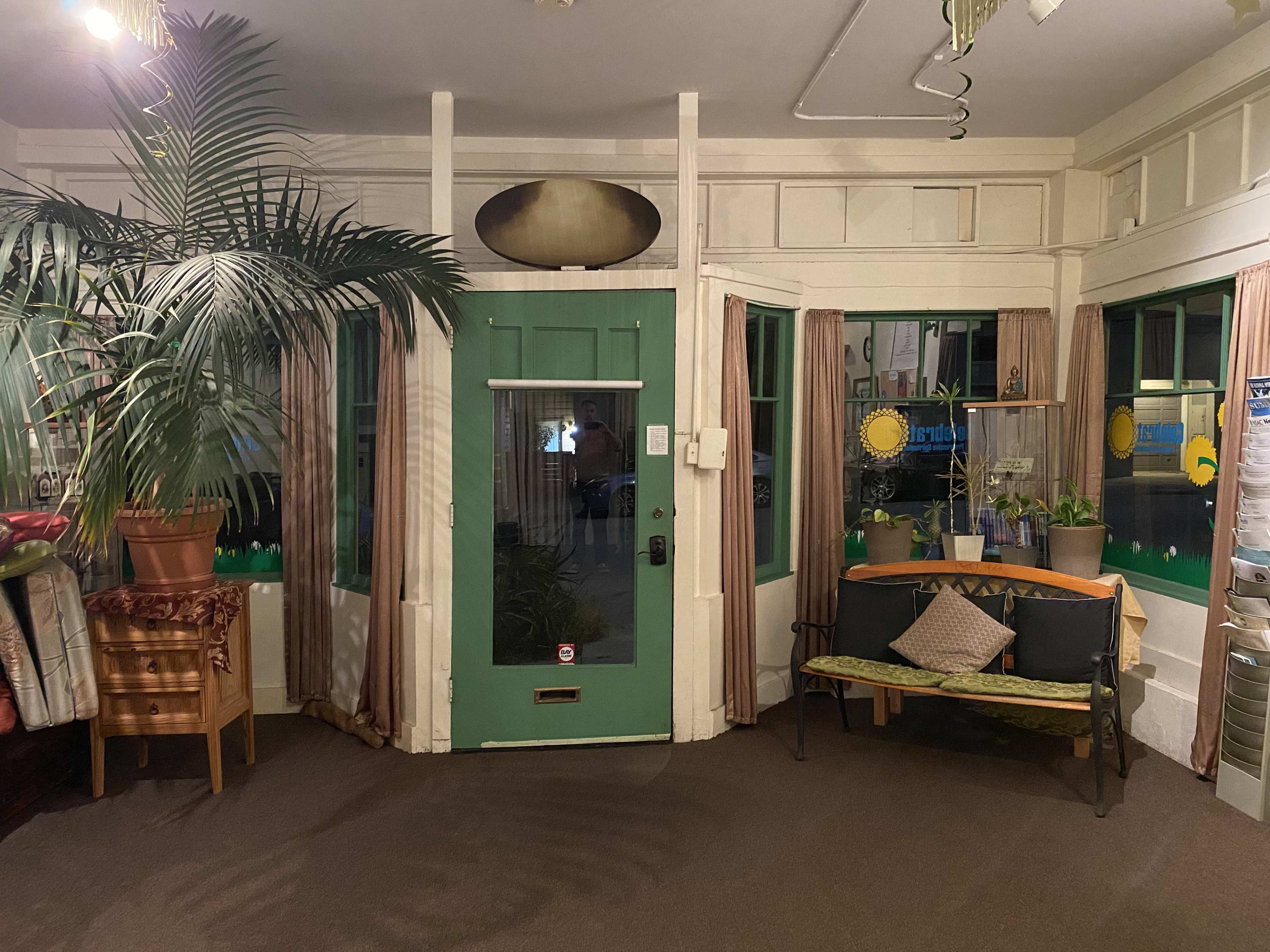 An interior space with a green door, large windows, a potted plant, and a small table with a chair against the wall.