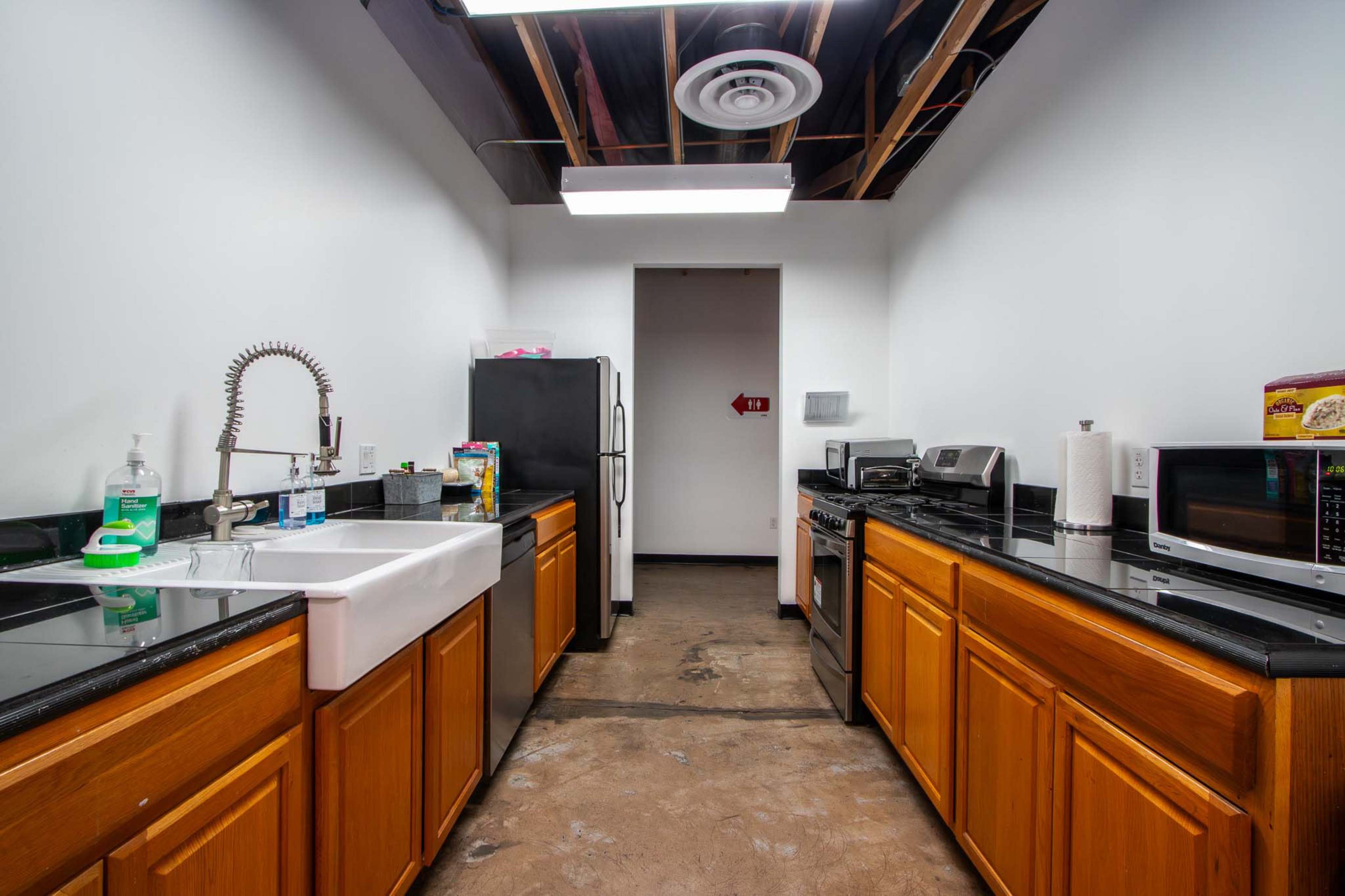 A kitchen featuring black countertops, wooden cabinets, a white farmhouse sink, and various appliances including a refrigerator, microwave, and toaster.