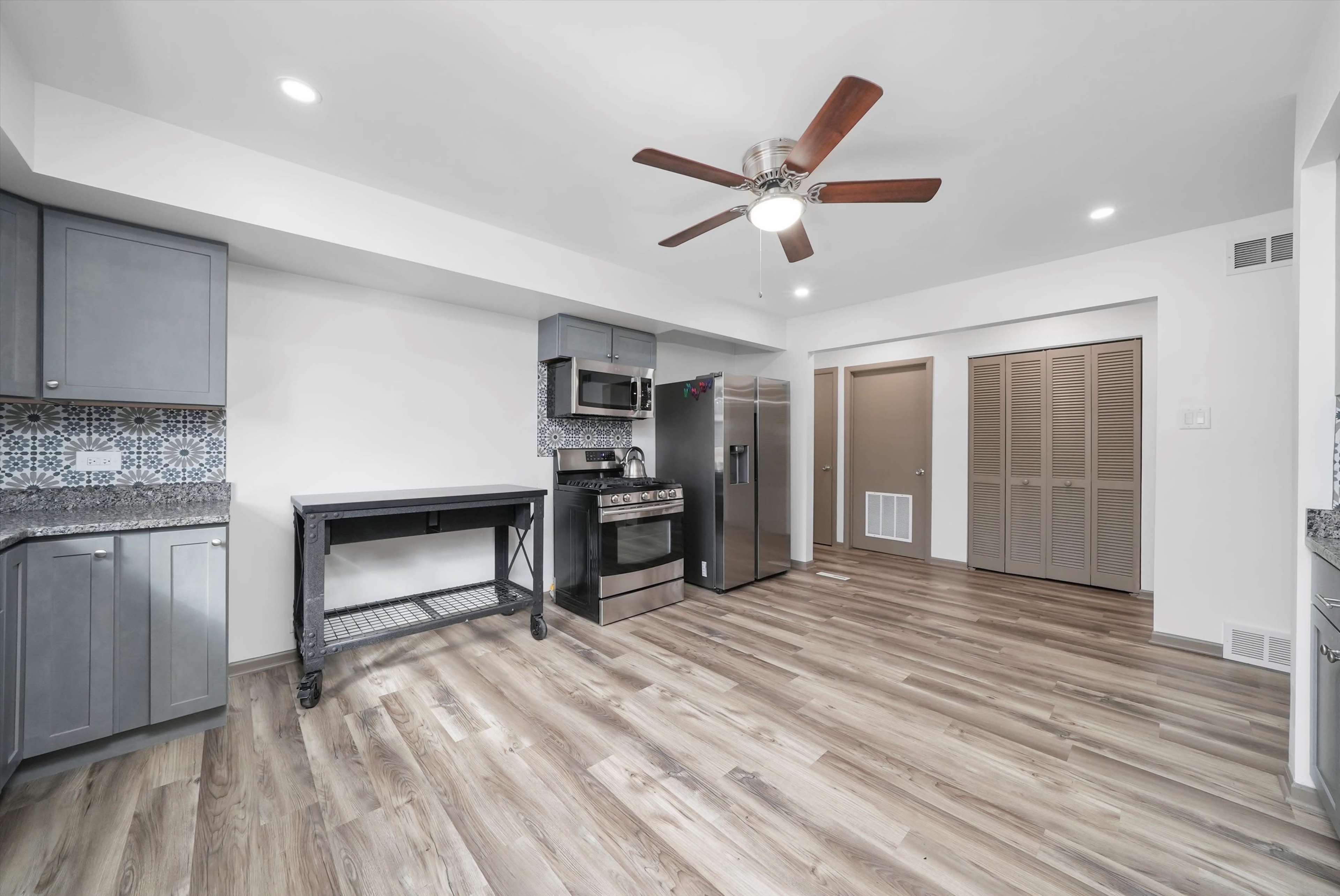 A modern kitchen with gray cabinets, stainless steel appliances, a ceiling fan, and laminate flooring.