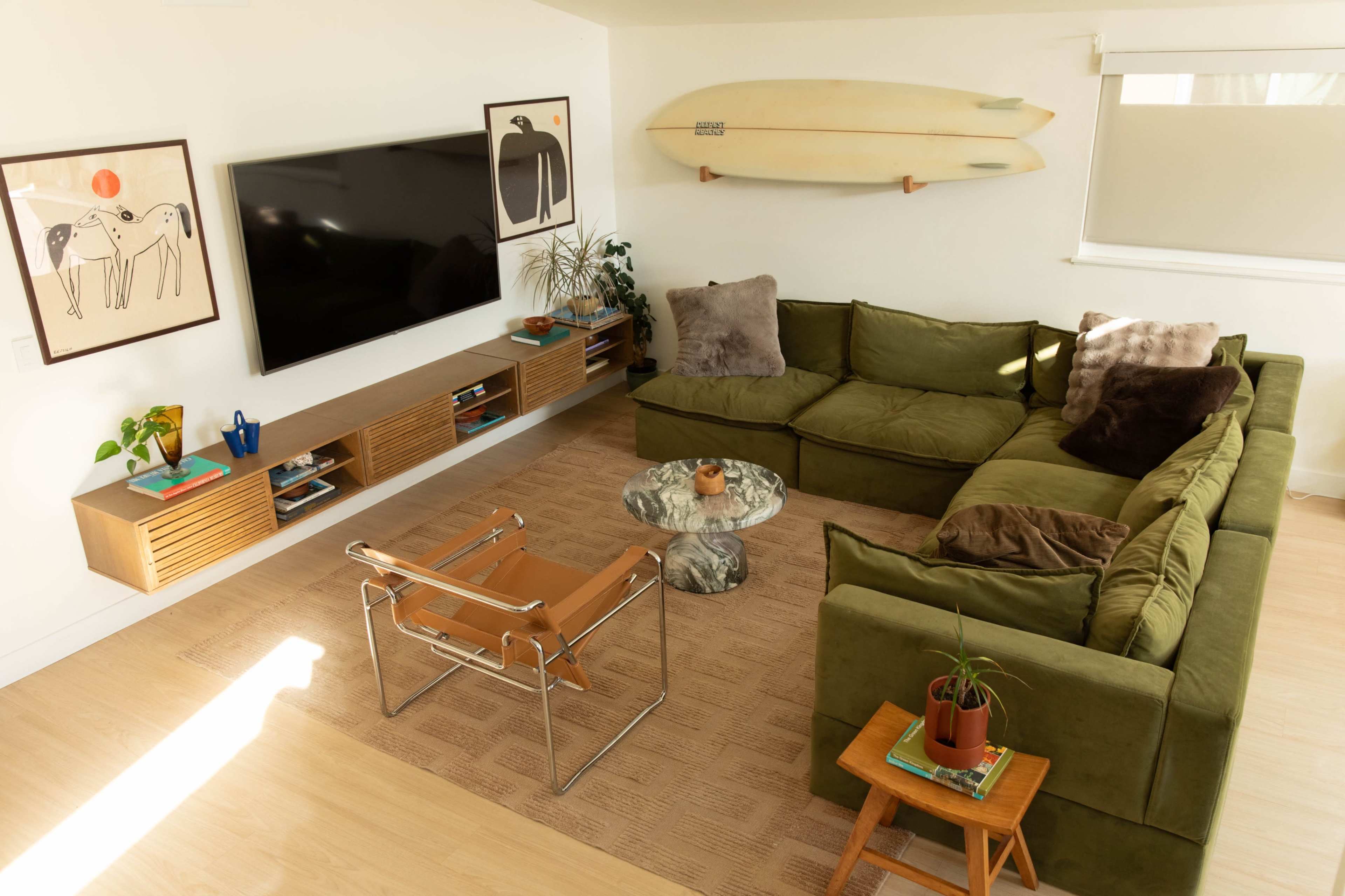 The living room features a large green sectional sofa, a coffee table, and decorative art on the walls, with a television and surfboards mounted above an entertainment unit.