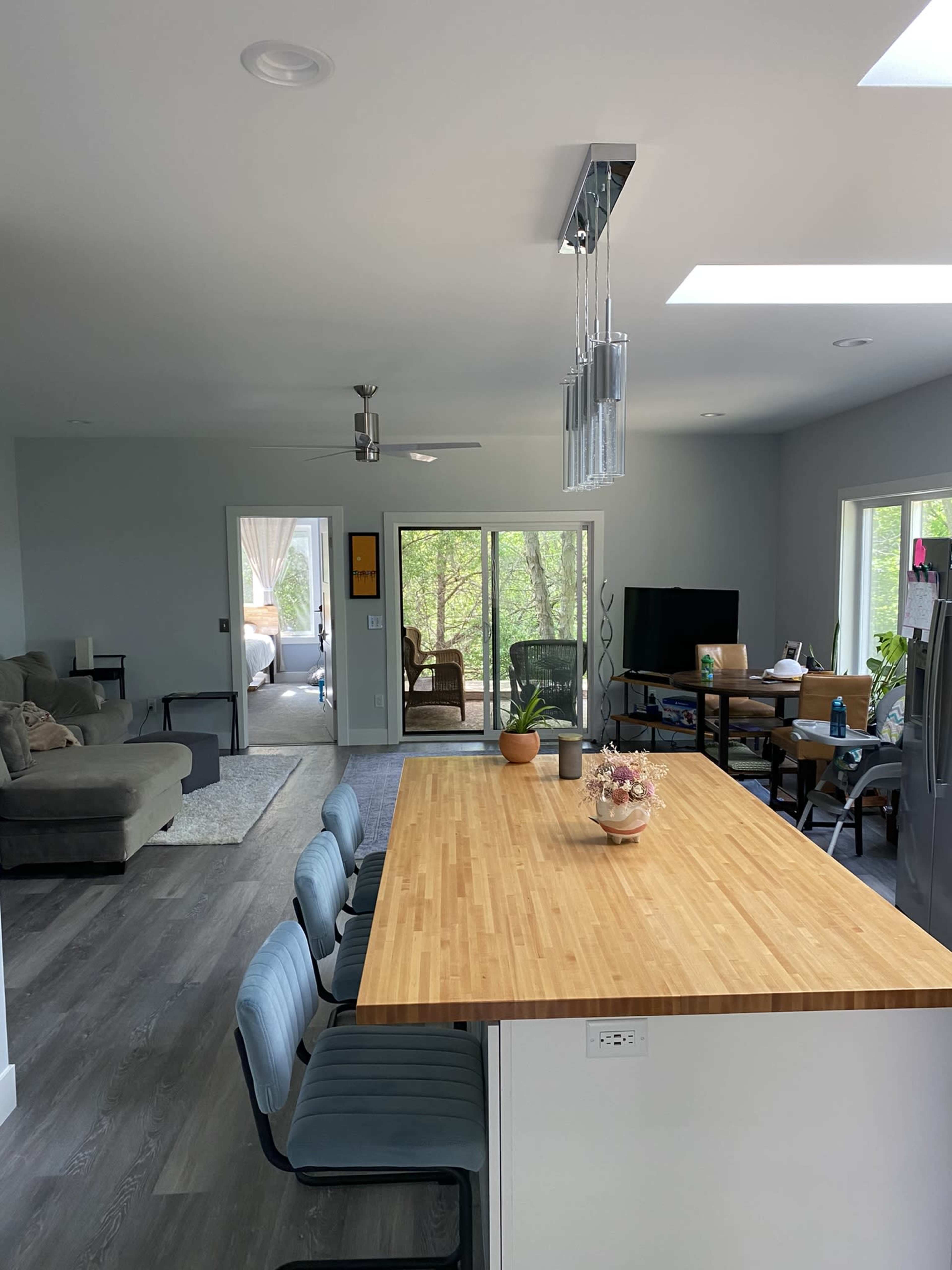A modern open-concept kitchen and living area with a large wooden island and seating, leading to a room with a couch and large windows.