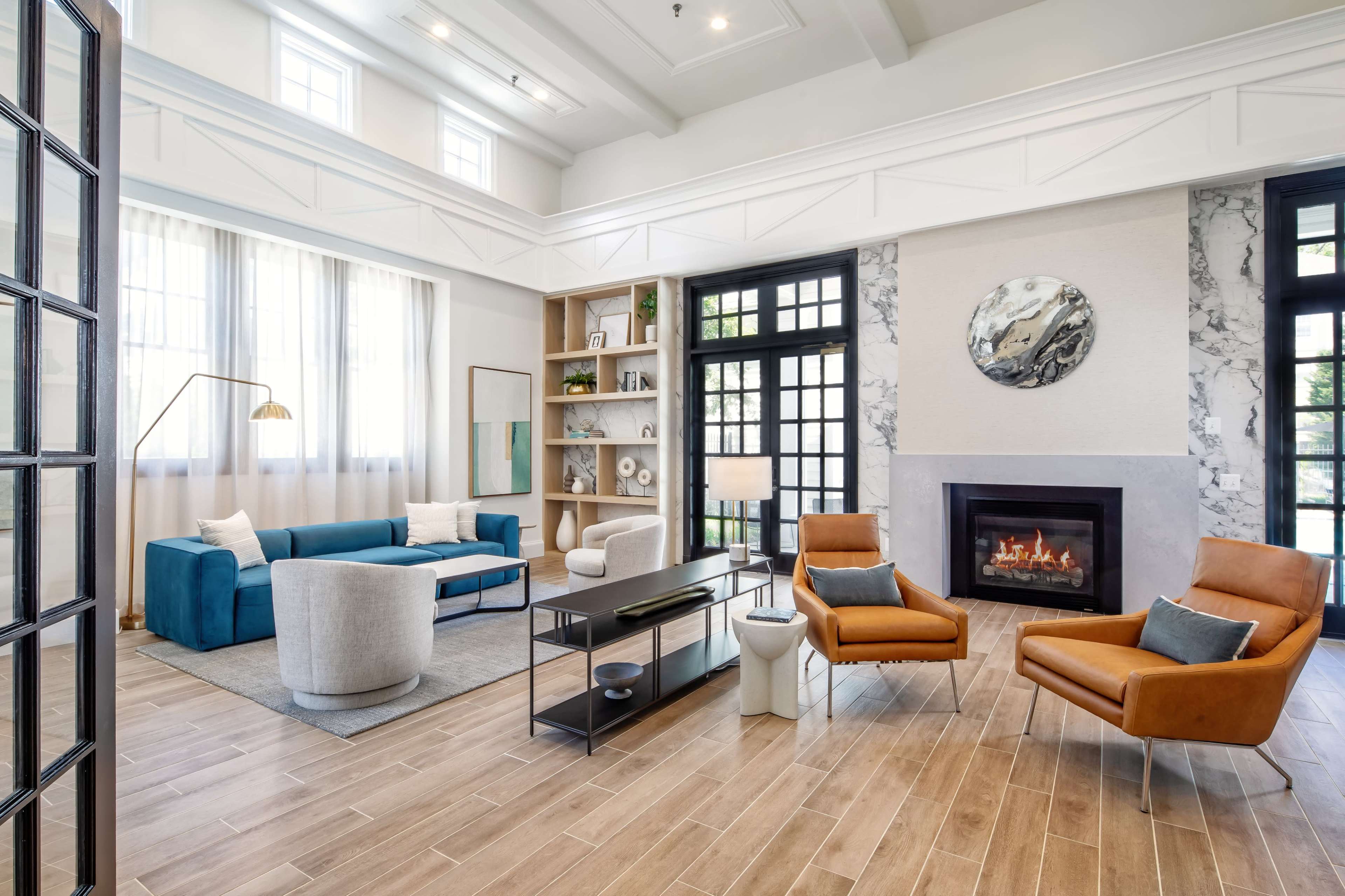 The image shows a modern living room with a fireplace, blue and gray seating, a coffee table, and large windows allowing natural light.