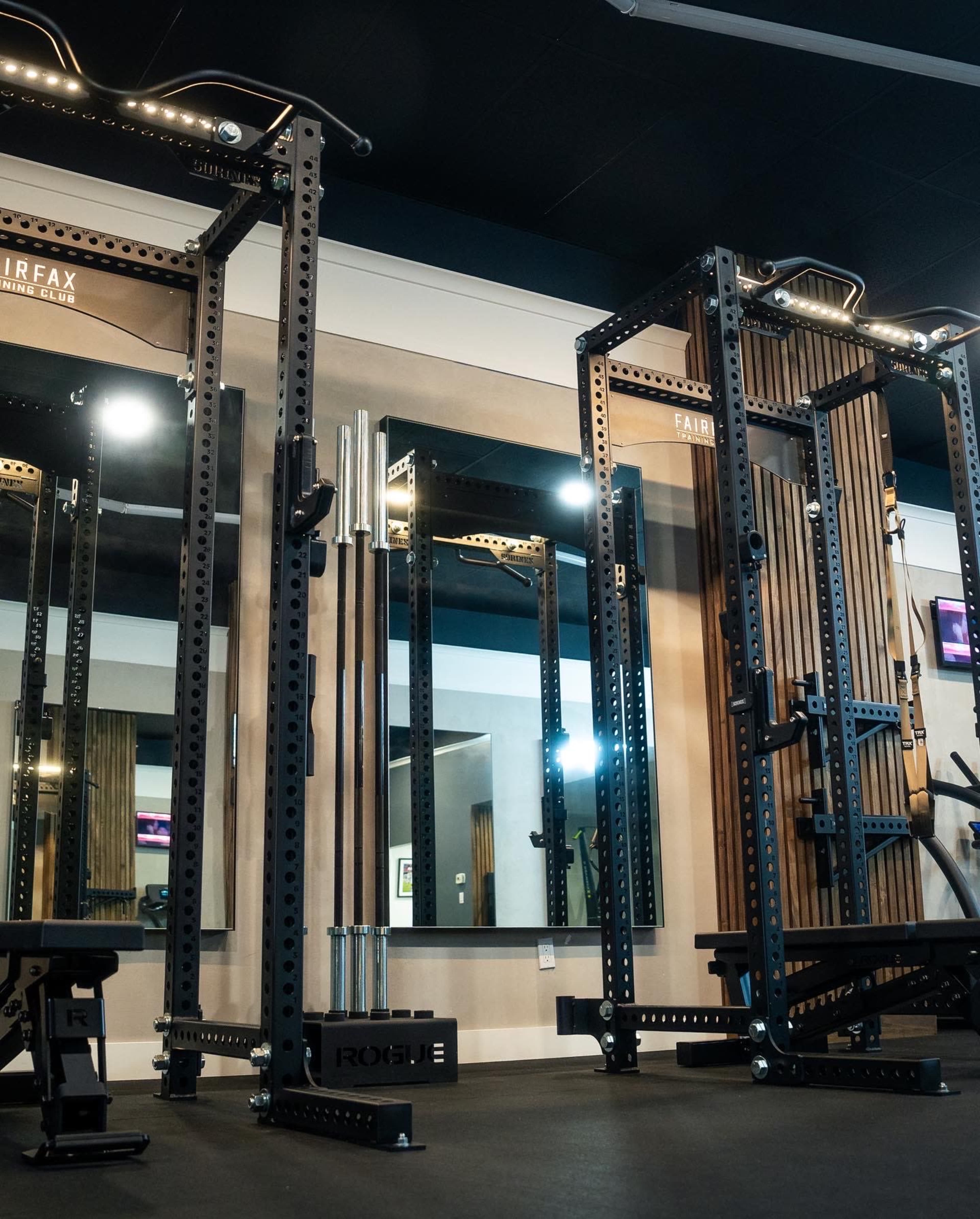 A well-equipped gym area featuring a squat rack, weightlifting bars, and mirrors on the walls.