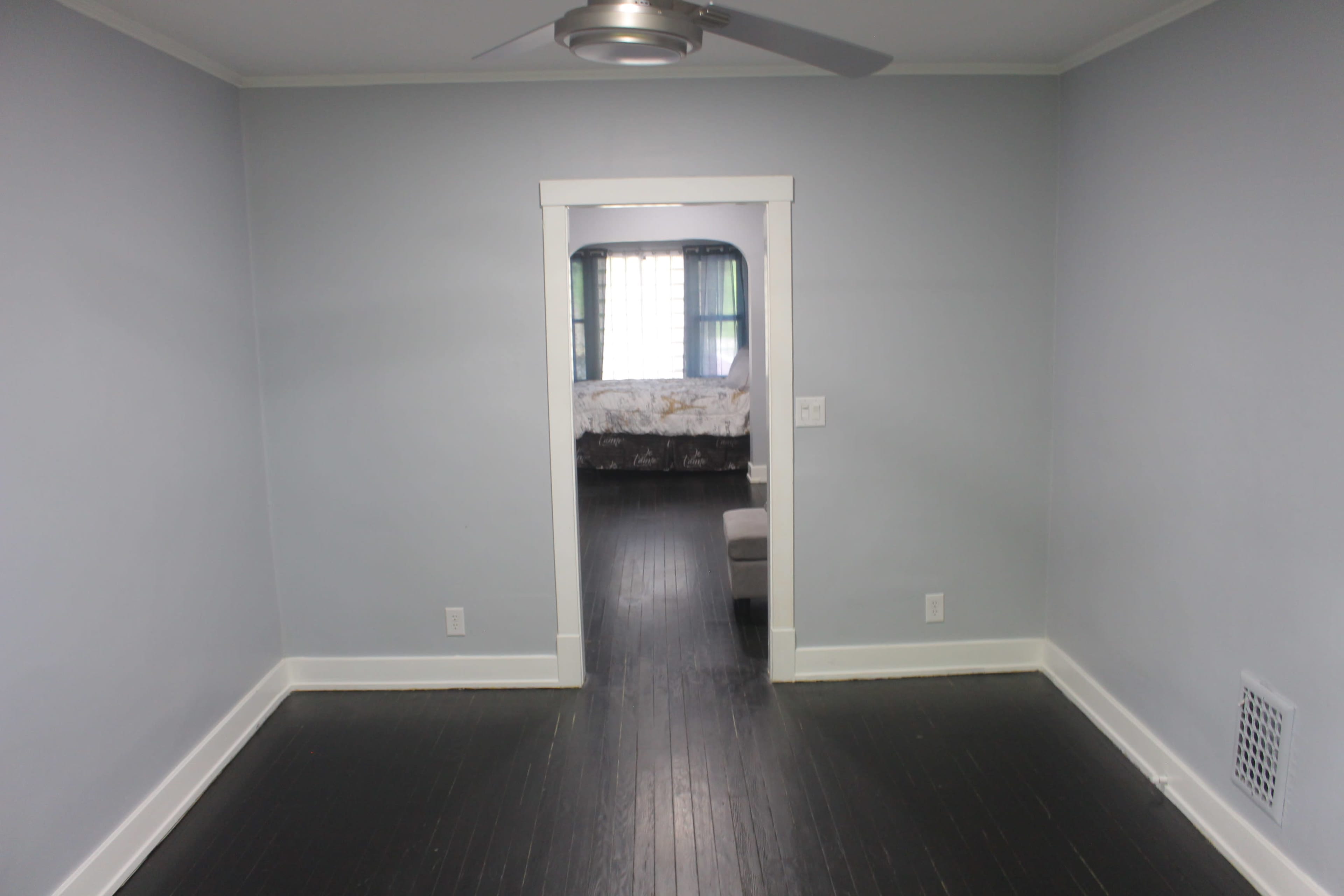 An empty room with gray walls, a ceiling fan, and a doorway leading to another room in the background.