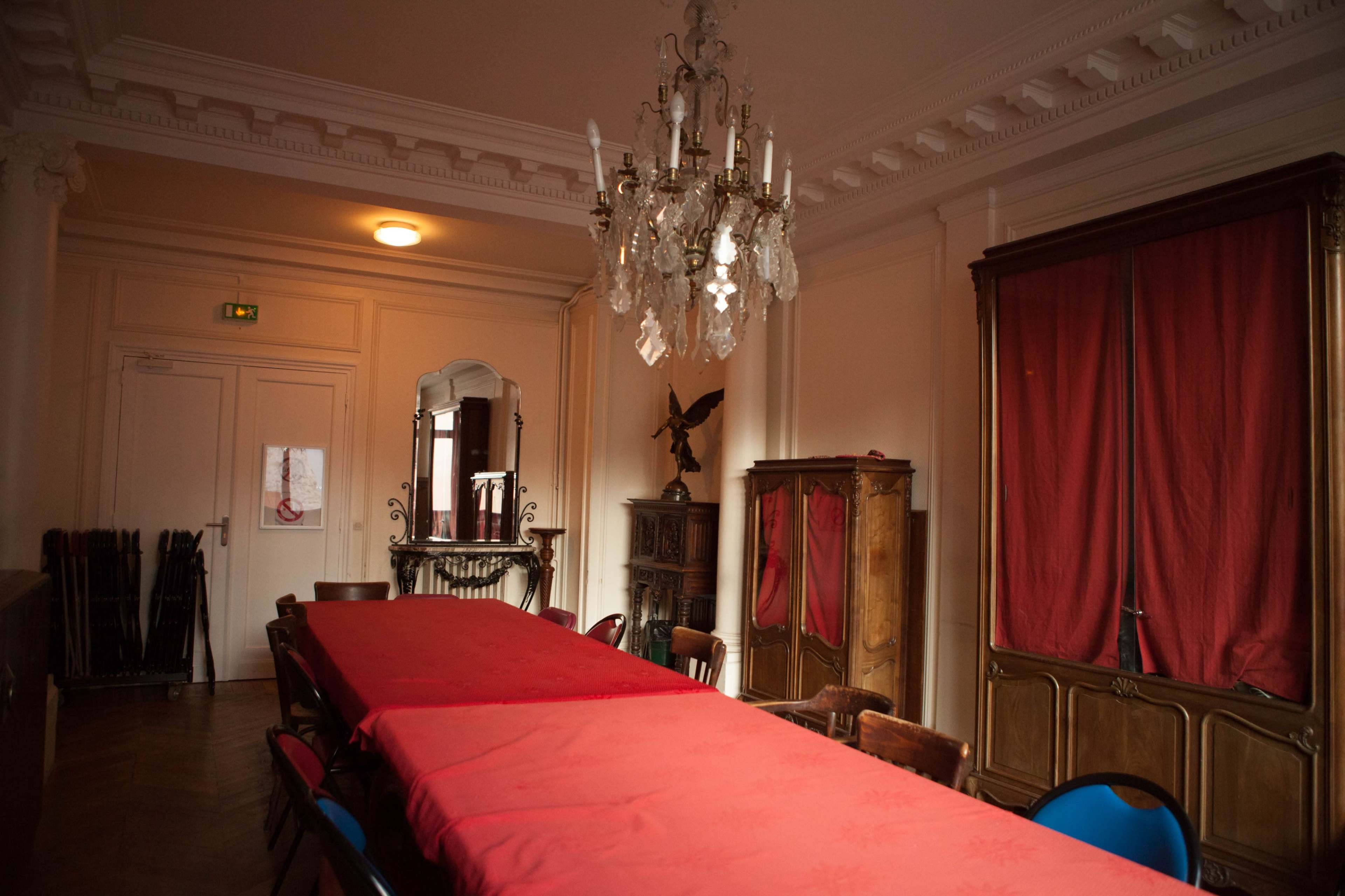 The image shows an elegantly decorated dining room with a long table covered in a red tablecloth, flanked by wooden chairs and featuring a chandelier overhead.