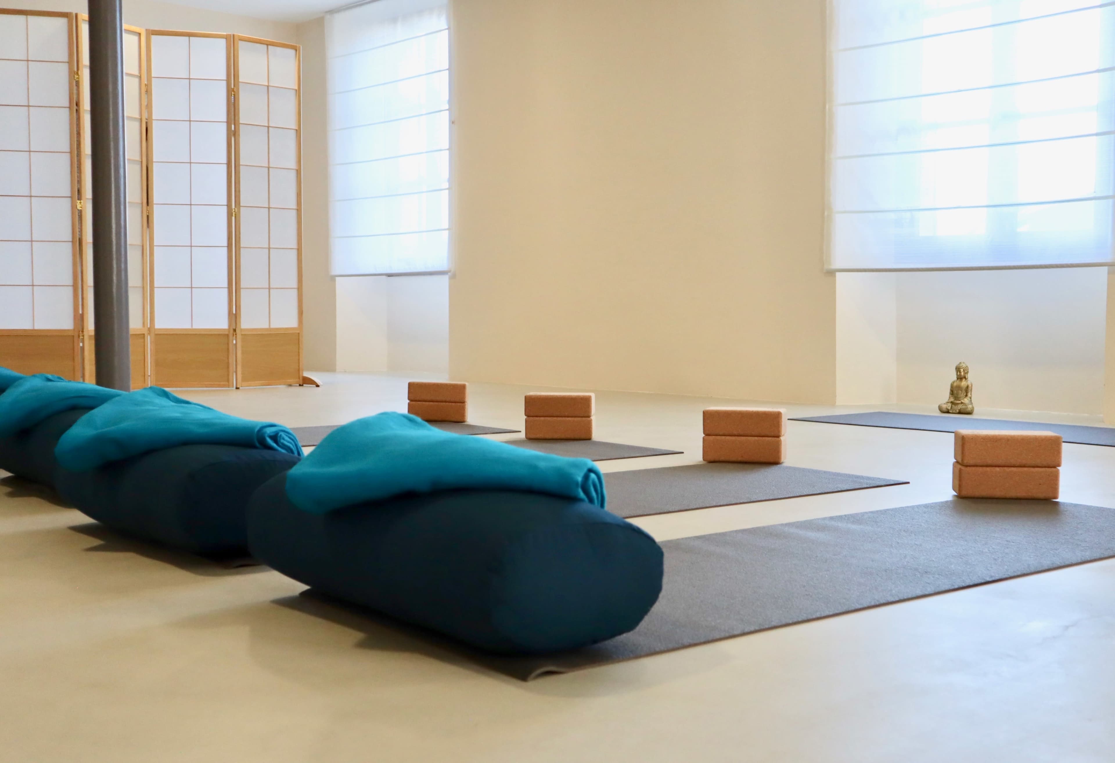 A serene yoga studio with blue bolsters, yoga mats, and wooden blocks arranged neatly, along with a small Buddha statue in the background.