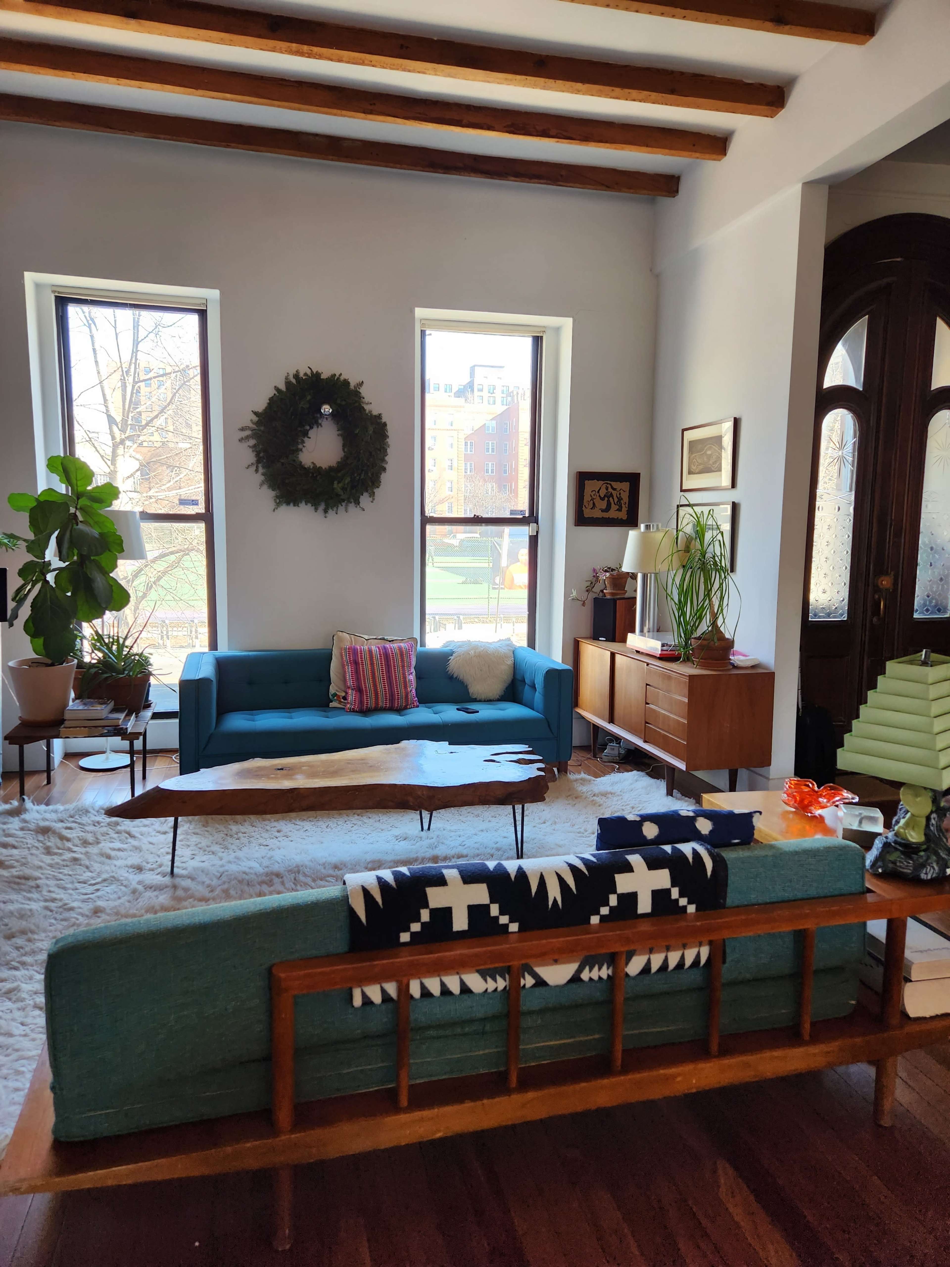 The living room features two couches, a coffee table, plants, and large windows overlooking an outdoor view.