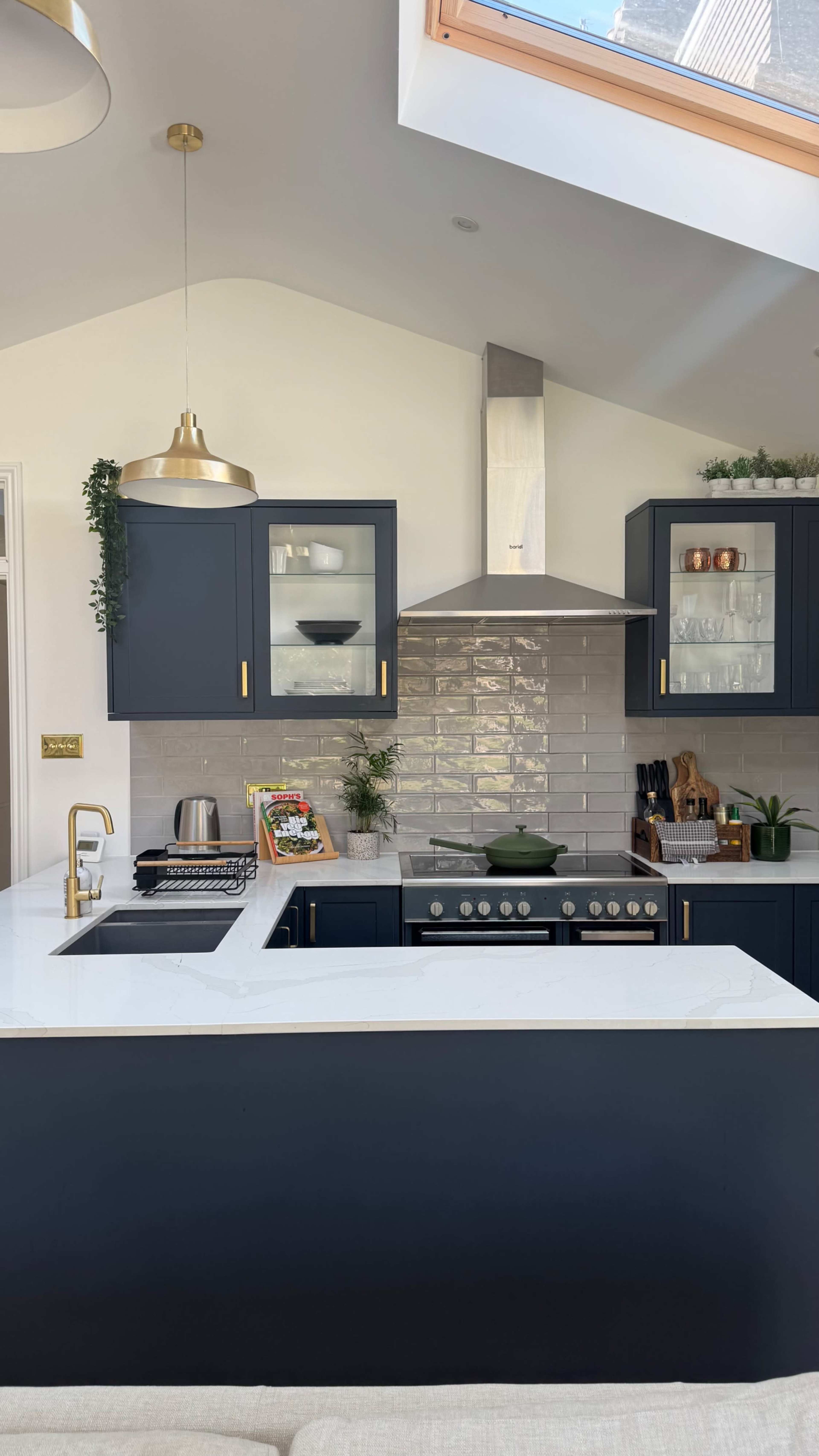 The image shows a modern kitchen featuring navy blue cabinets, a stainless steel range hood, and a white marble countertop with a sink and various kitchen appliances.