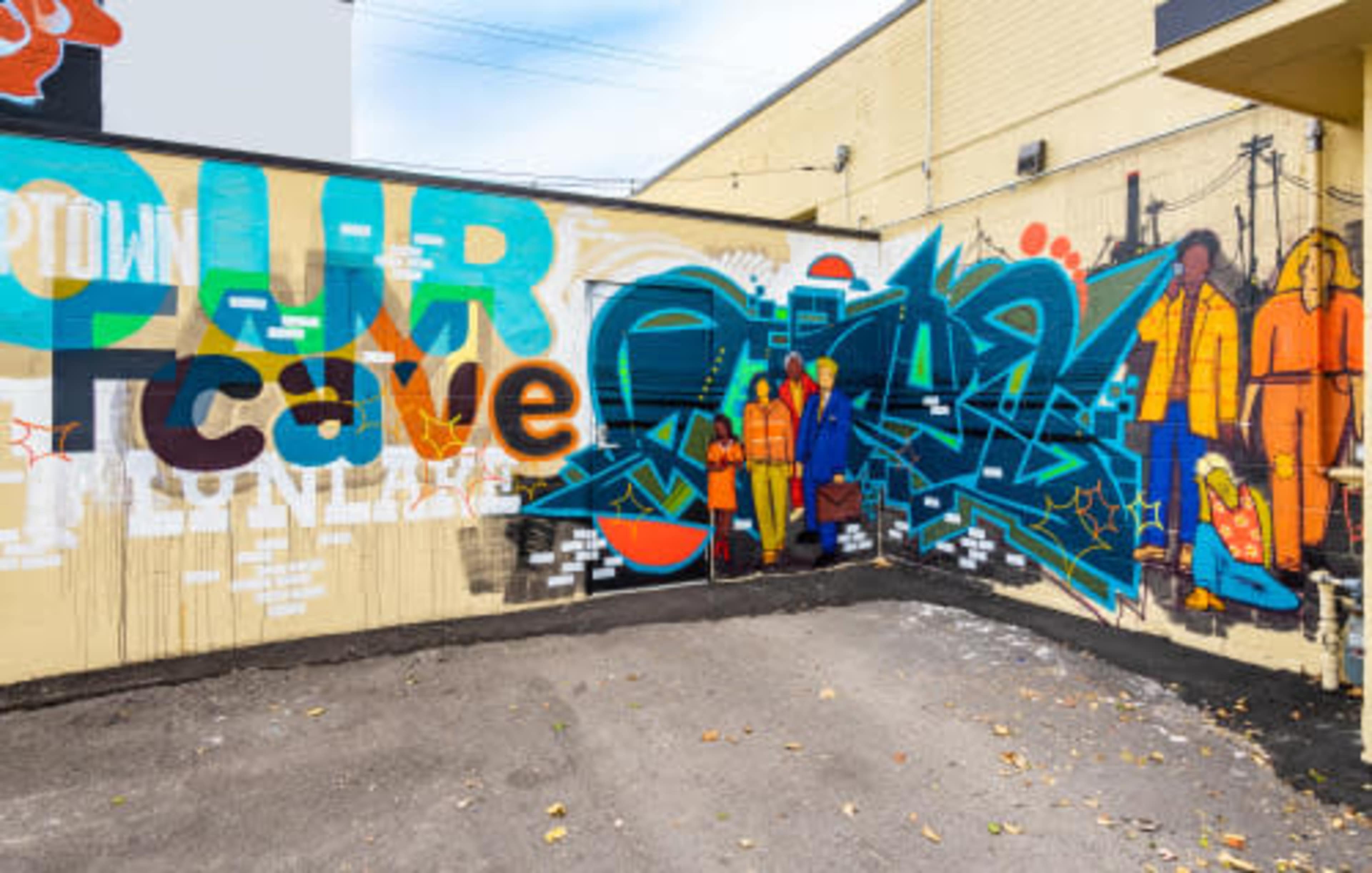 A colorful mural on a wall featuring vibrant graffiti and figures, alongside the text "OUR CAVE."