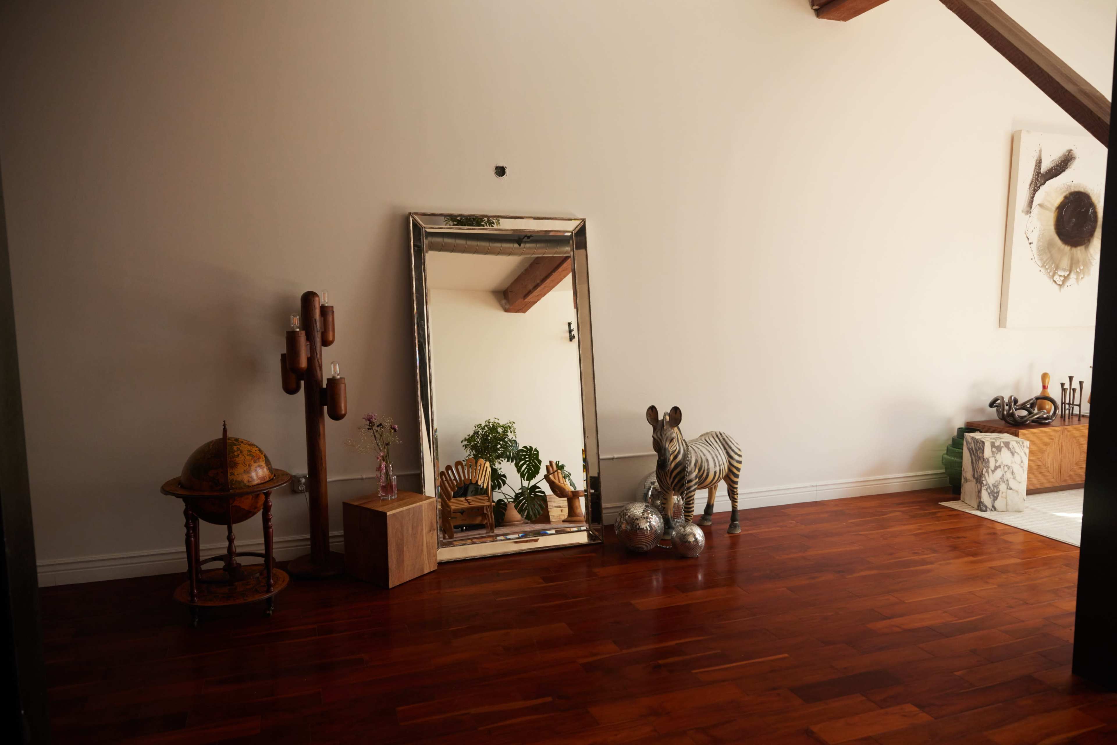 A large mirror reflects the interior of a room featuring a zebra sculpture, a globe on a stand, and potted plants.