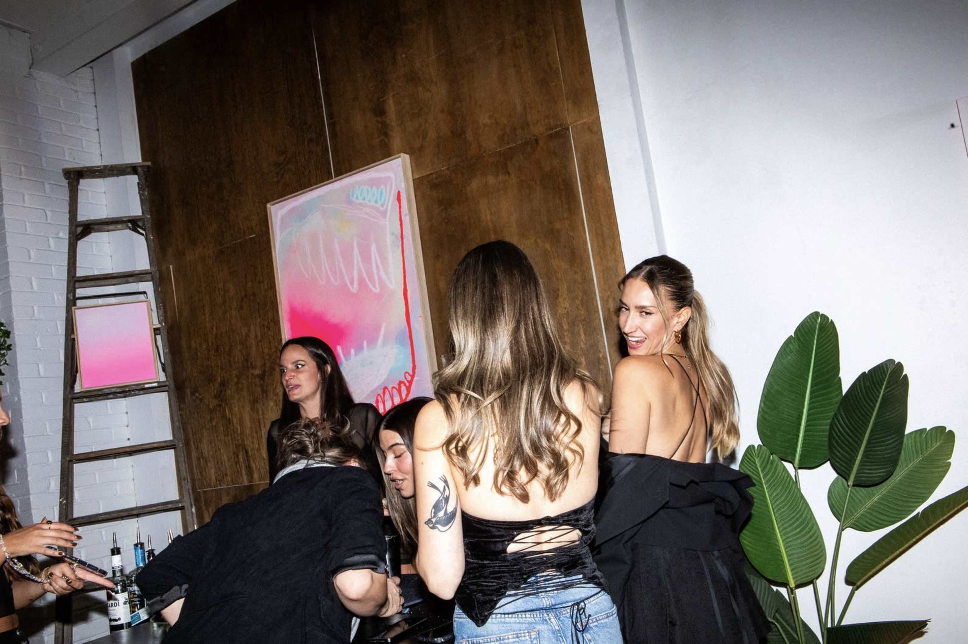 A group of people socialize in a modern interior with a wooden wall and a colorful artwork.