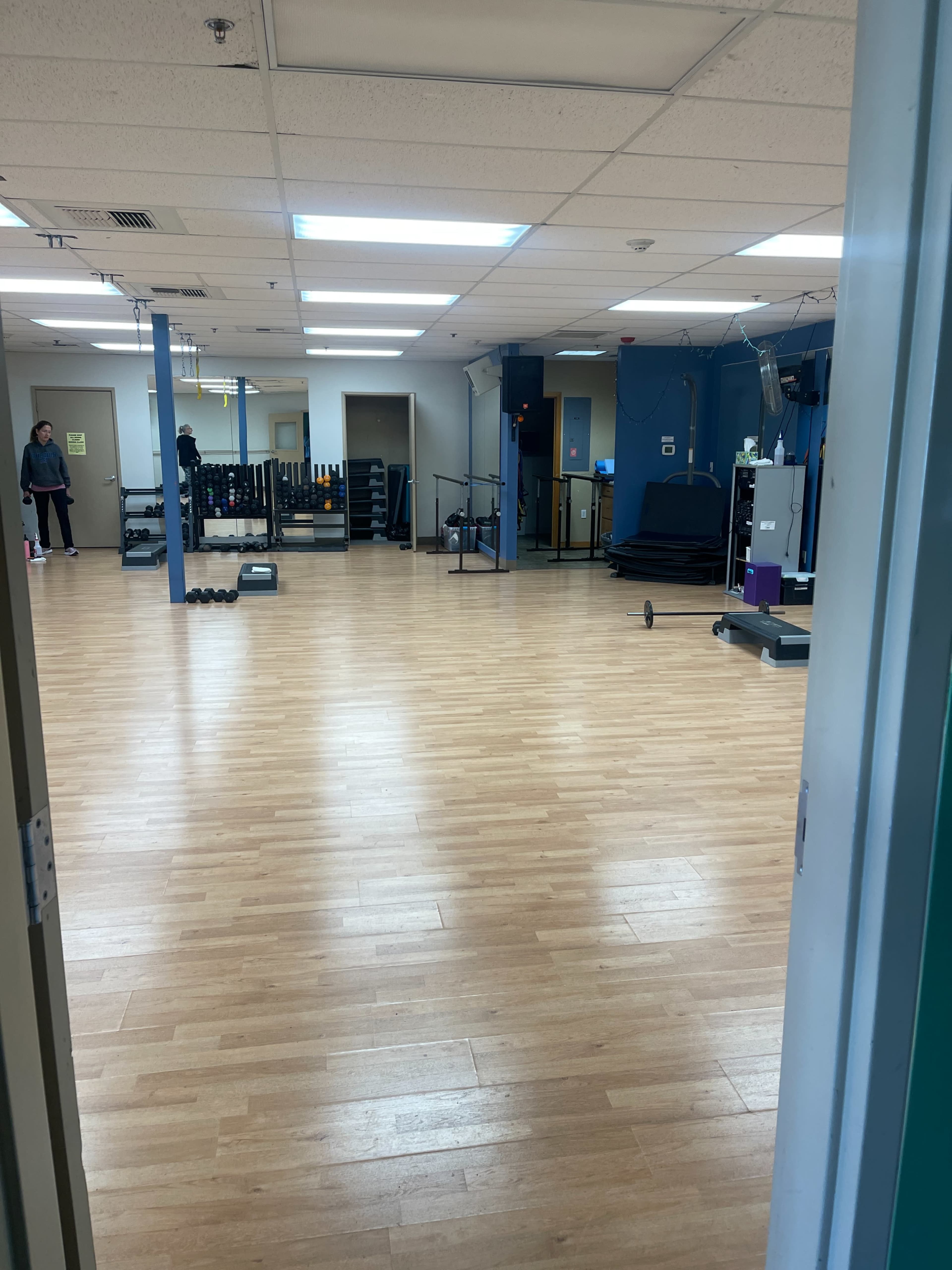 A fitness studio with wooden floors and various exercise equipment is visible through an open doorway.