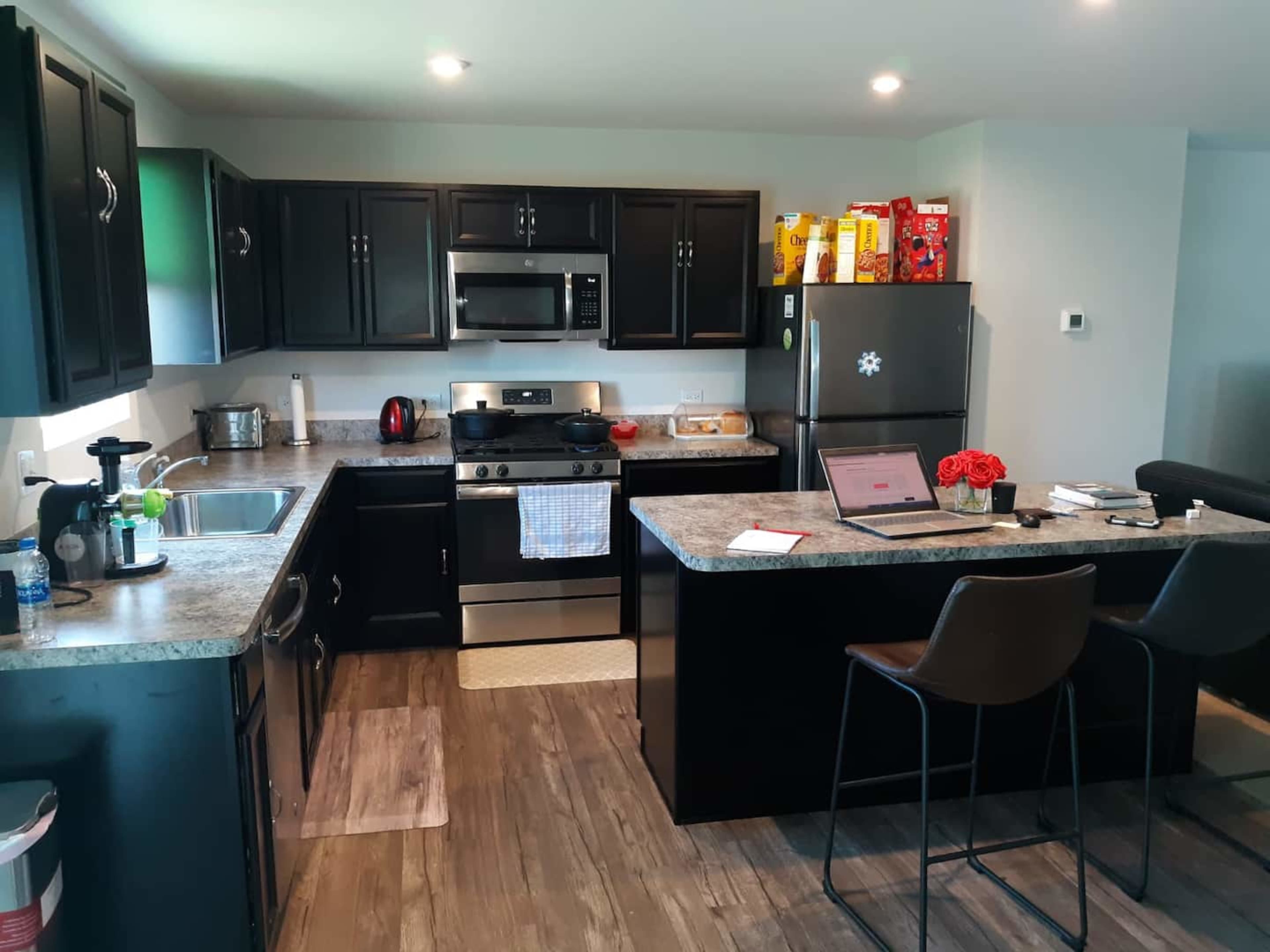 A modern kitchen featuring dark cabinetry, stainless steel appliances, and a dining island with seating.