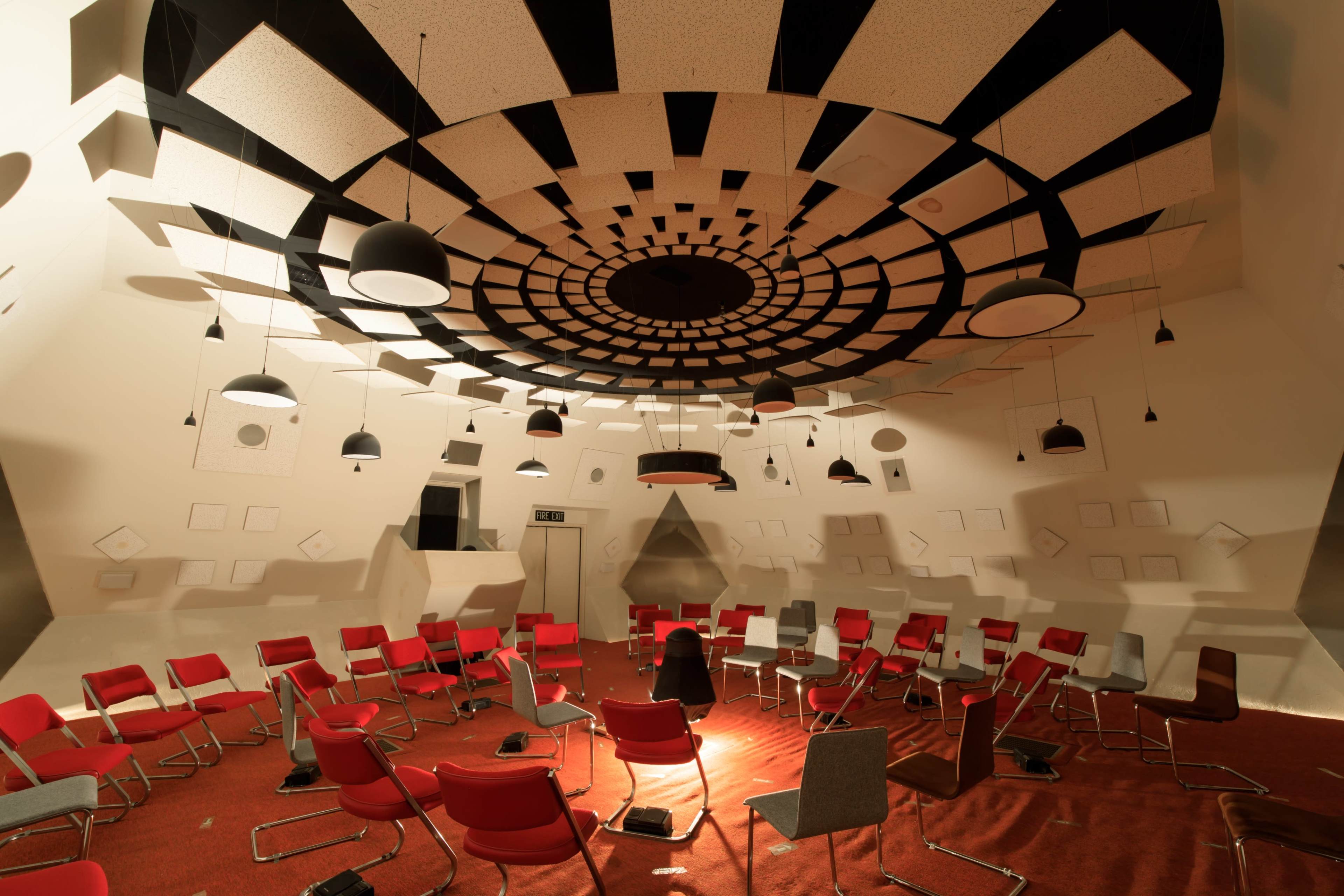 The image shows a circular room with a patterned ceiling, featuring red and gray chairs arranged in a circular formation on a carpeted floor.