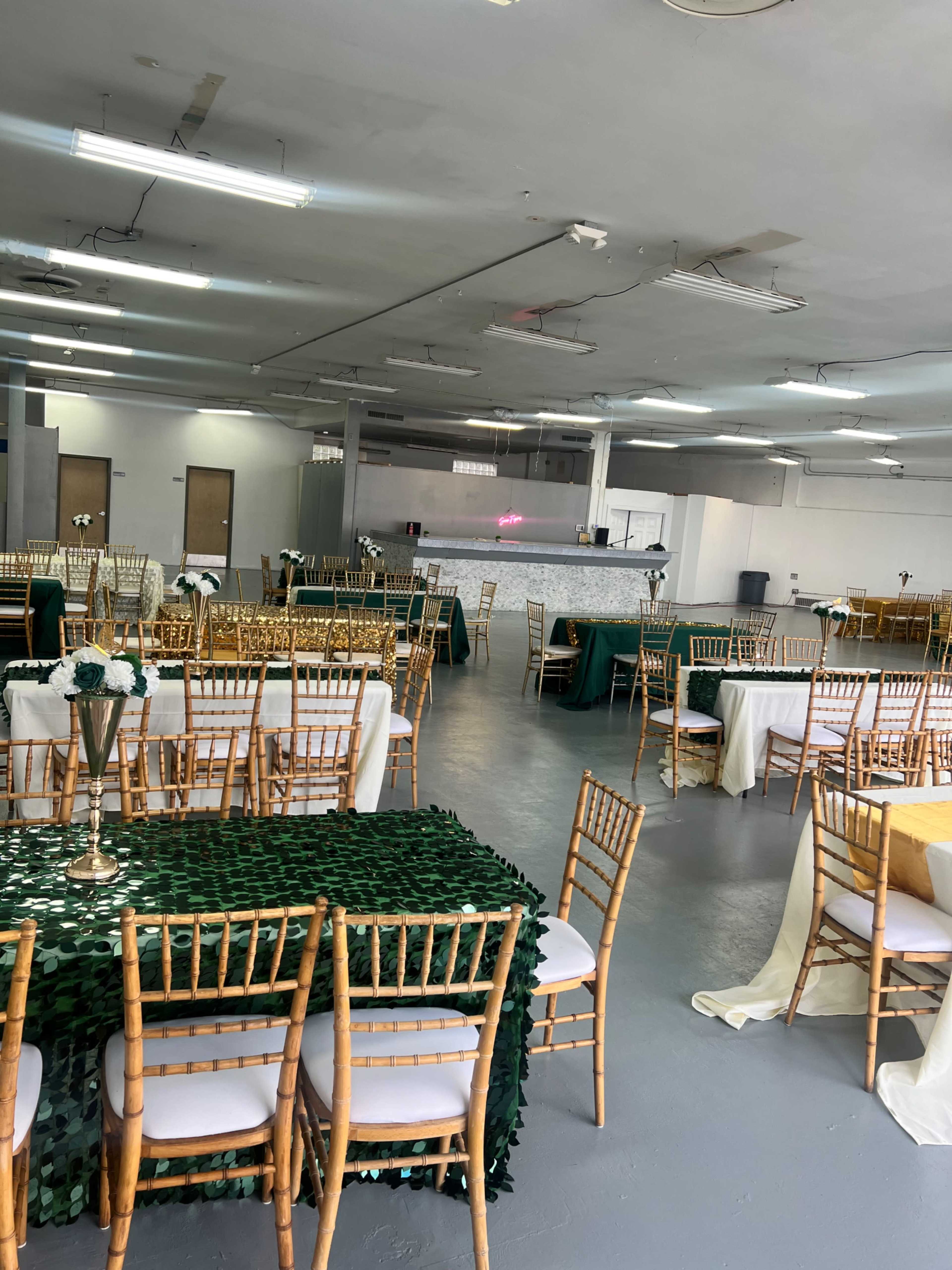 A spacious banquet hall arranged with multiple tables covered in various colored tablecloths and set with chairs facing a serving area.
