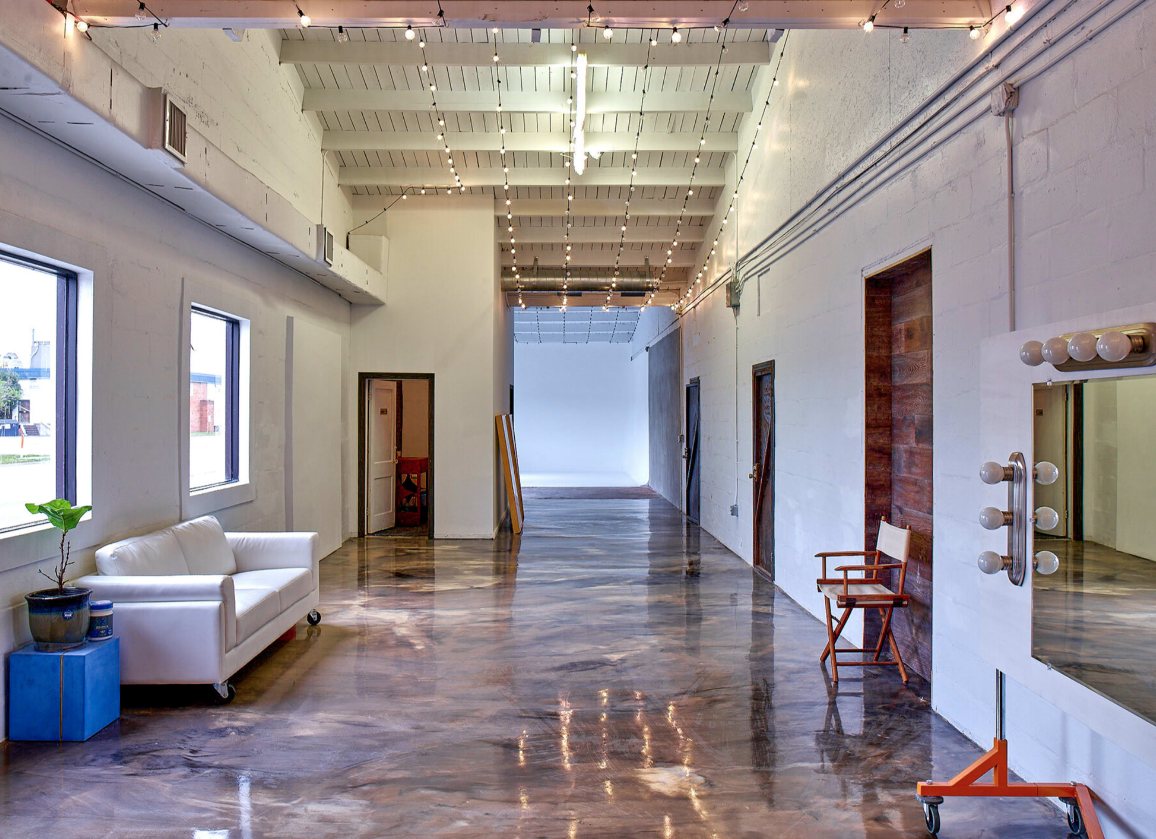 A spacious, well-lit interior corridor with polished concrete floors, large windows, and decorative string lights above.