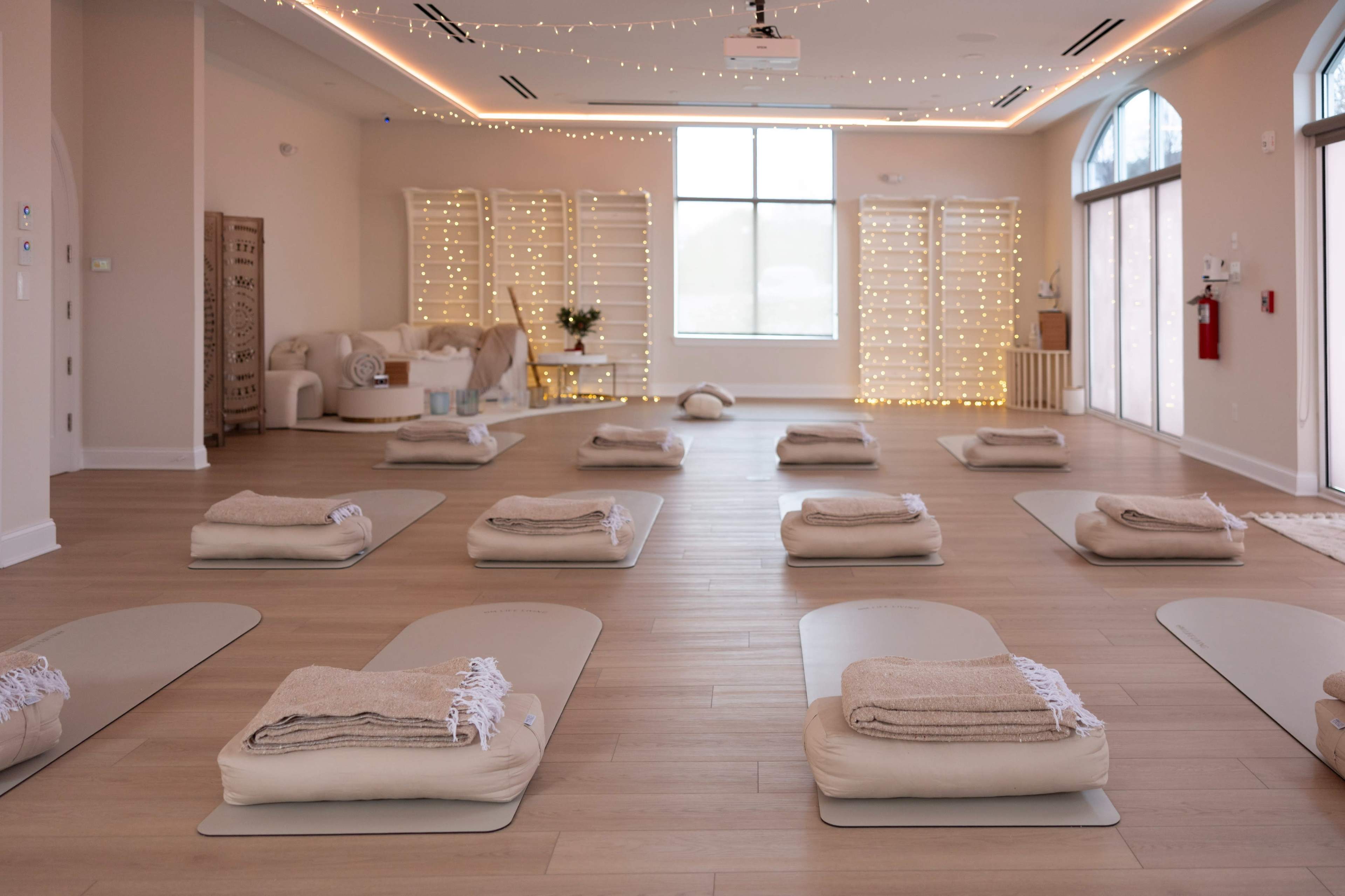 The image shows a serene yoga studio with neatly arranged mats and cushions, soft lighting, and decorative elements in the background.