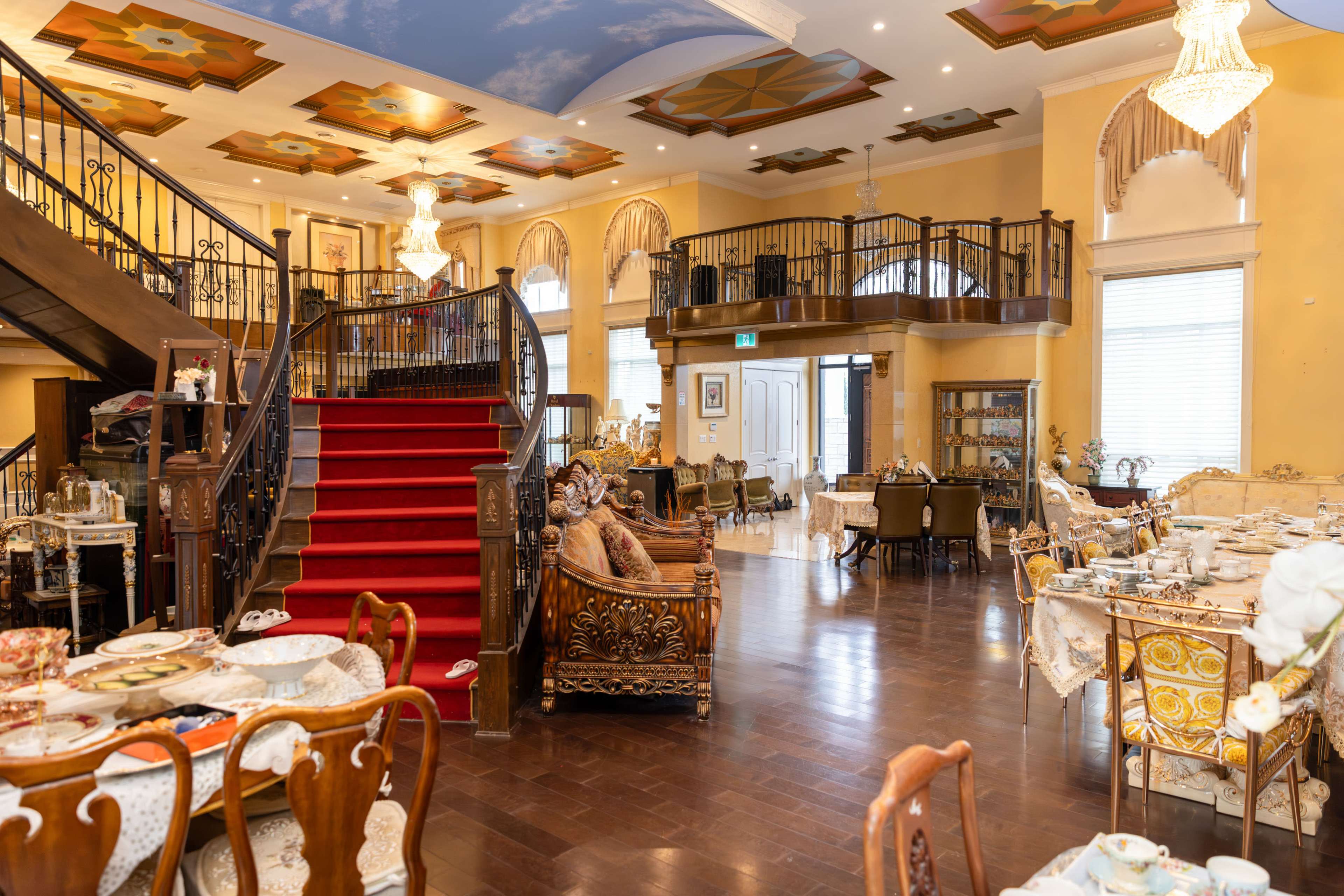 The image shows an elegantly decorated restaurant featuring a grand staircase, ornate chandeliers, and a variety of dining tables arranged throughout the space.