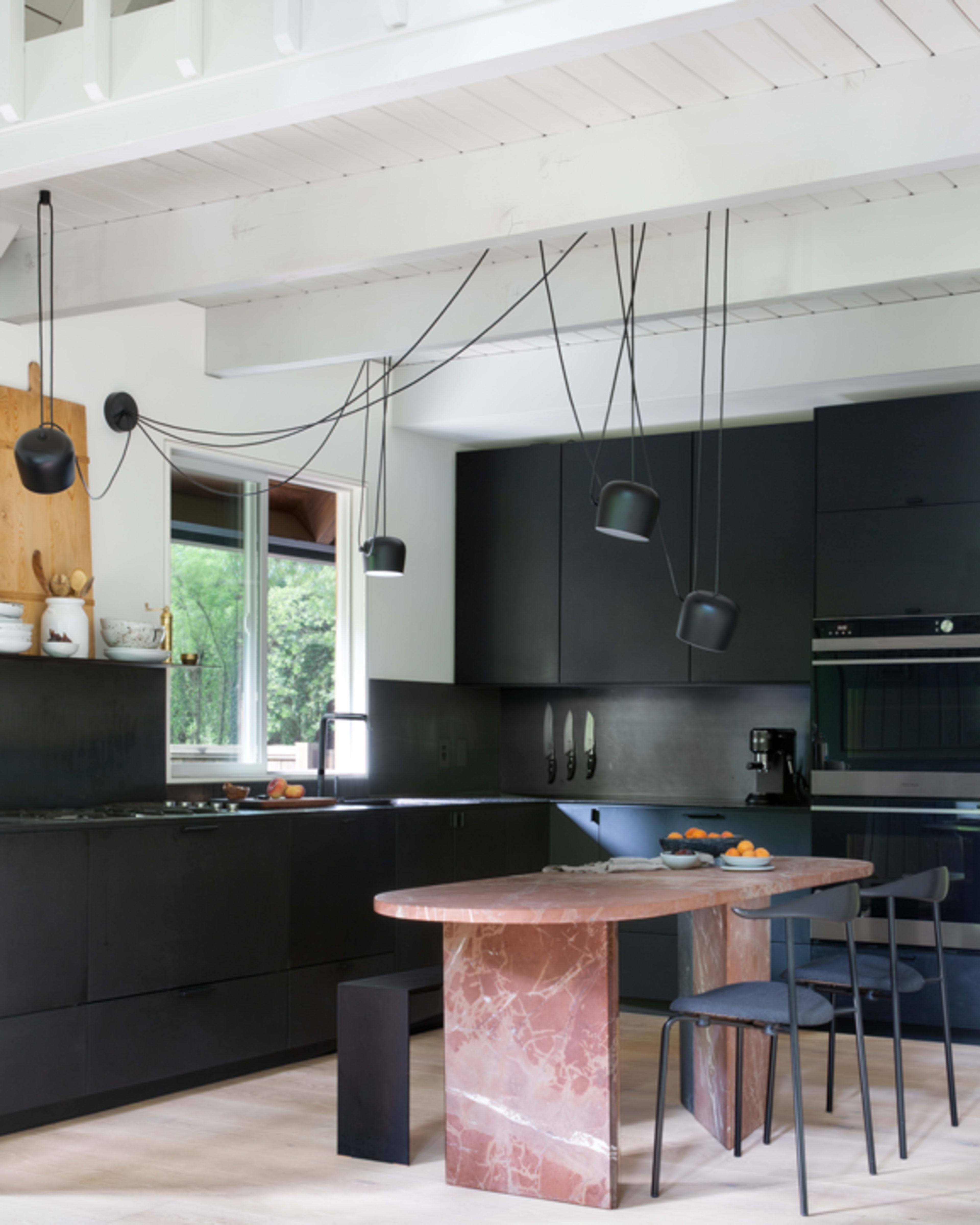 The image shows a modern kitchen featuring black cabinetry, a pink marble island, and pendant lights hanging from the ceiling.