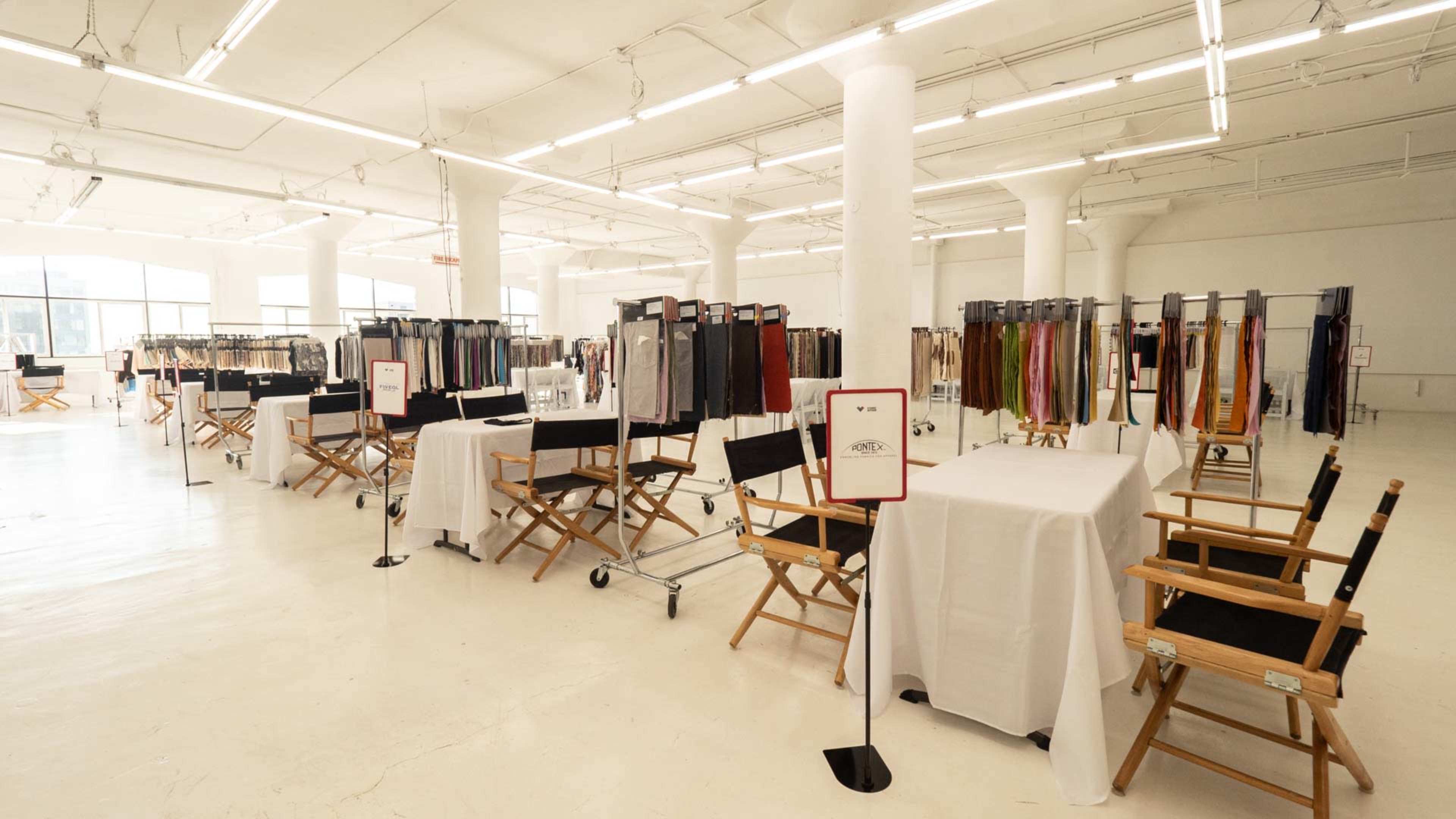 A spacious room filled with display racks of various clothing items and several director's chairs arranged around tables.