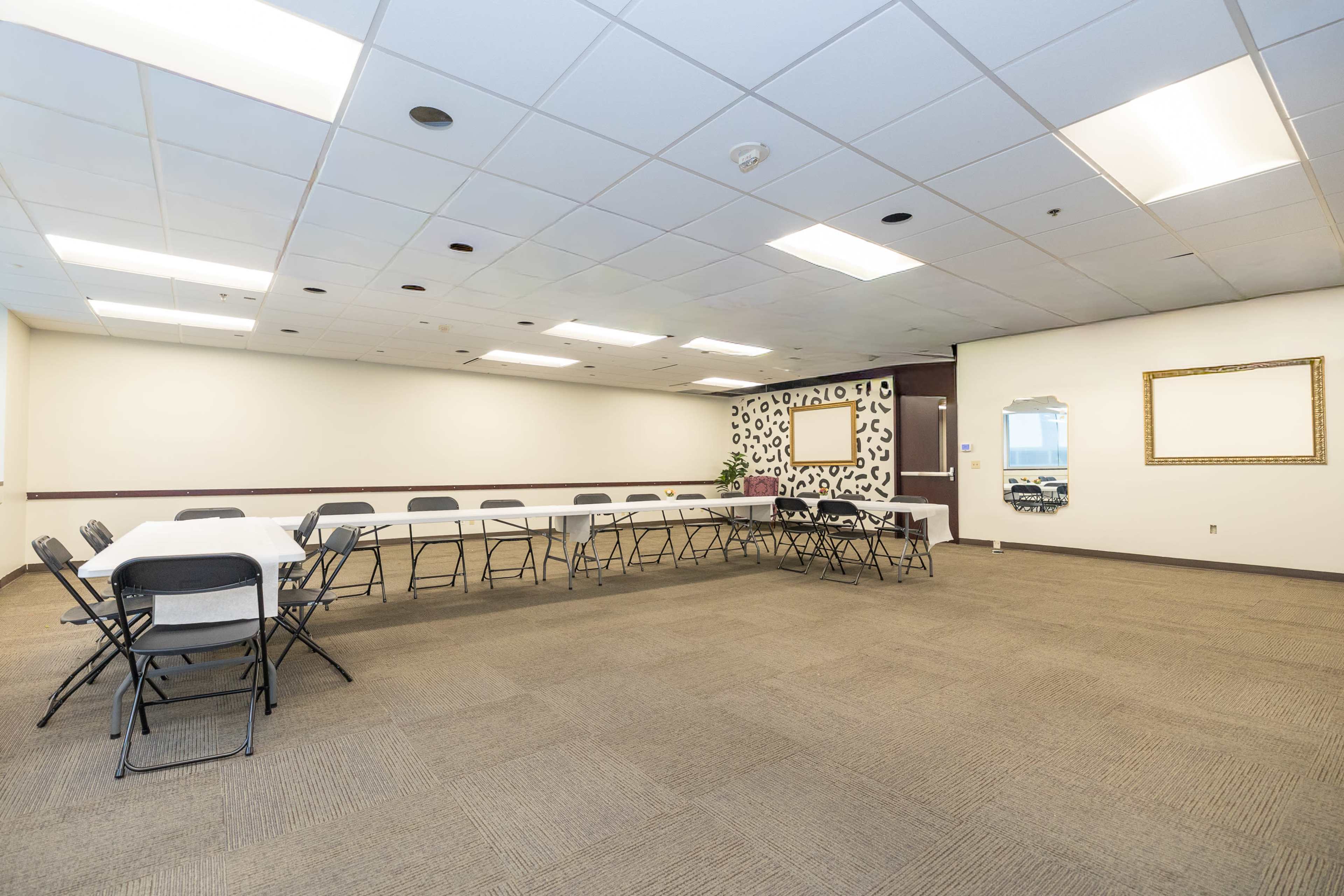 A spacious meeting room features several tables arranged in a U-shape and is equipped with chairs, along with decorative elements on the walls.