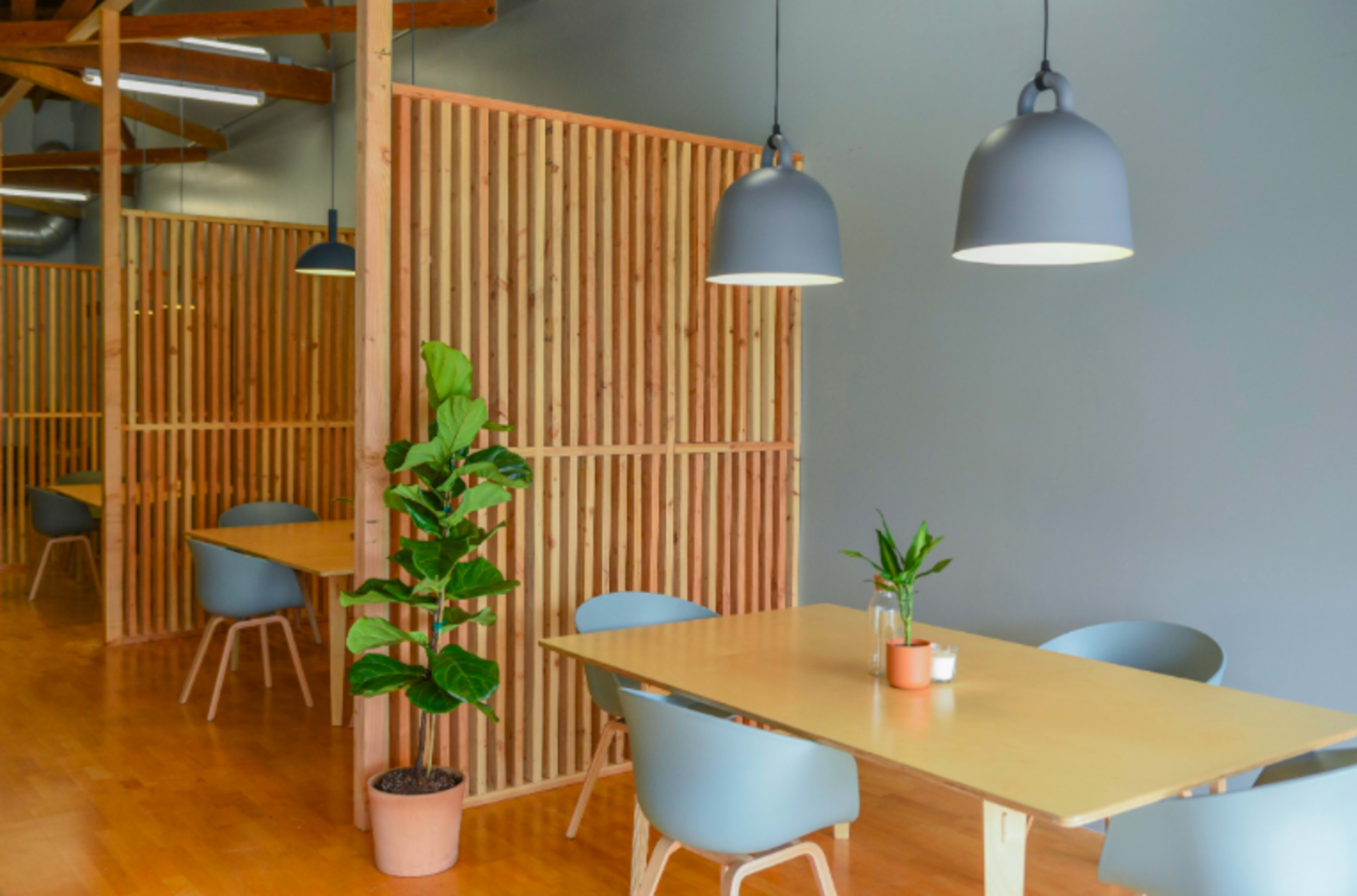 A modern interior space with wooden flooring, partitioned seating areas, and potted plants under pendant lighting.